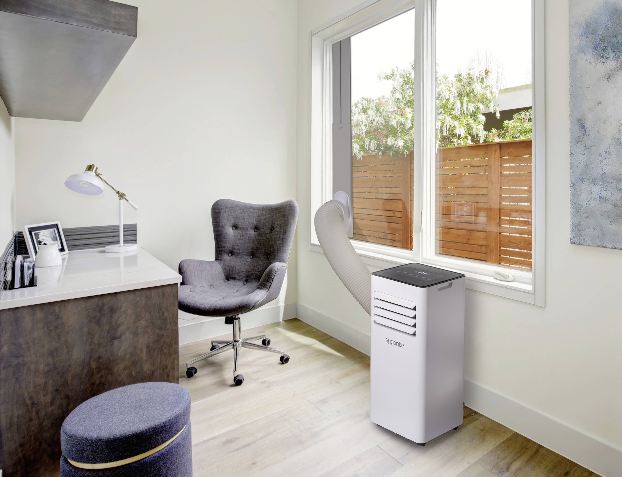 Een moderne, lichte werkruimte met een gezellige fauteuil, bureau en een mobiele airconditioning naast het raam.