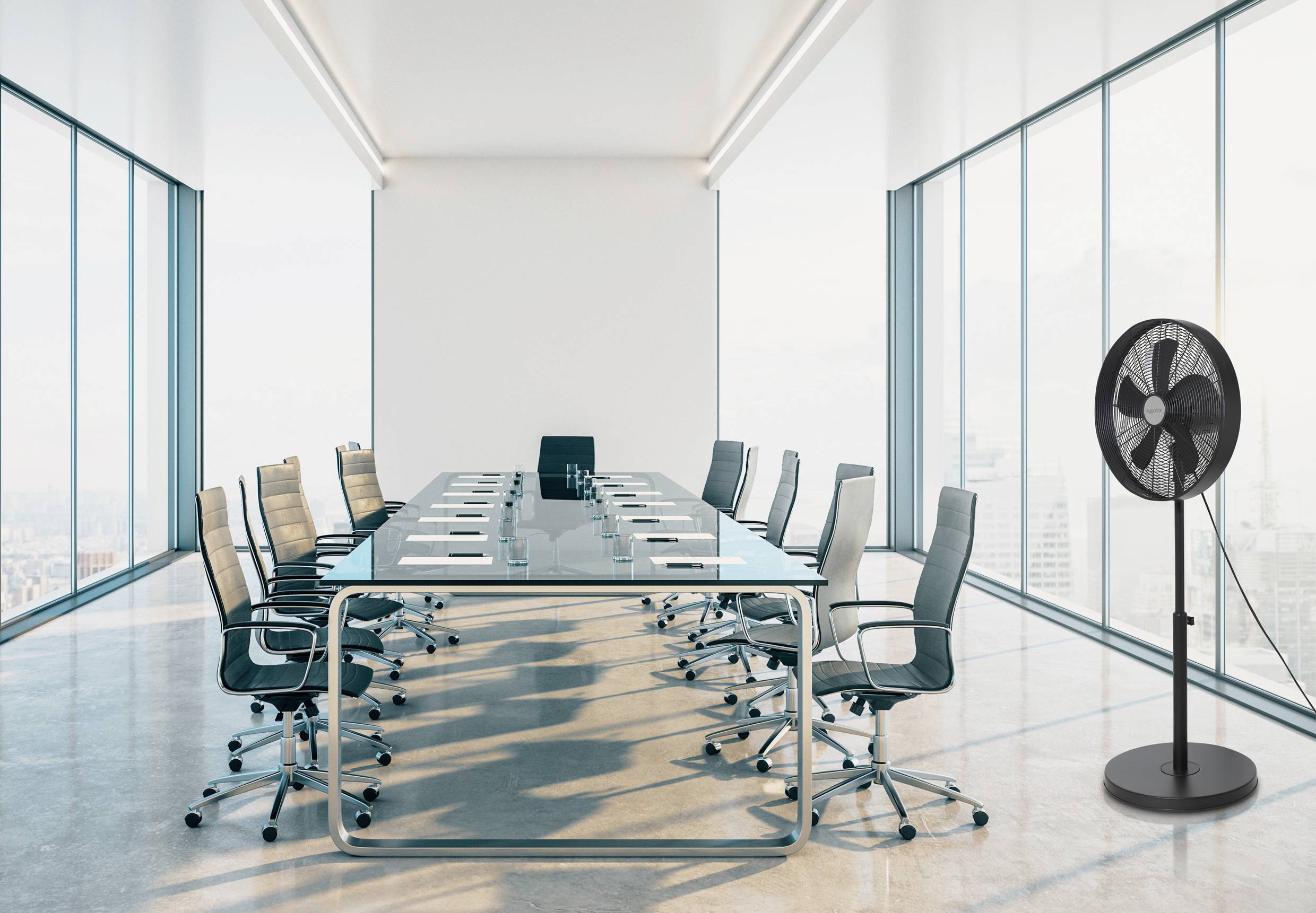 Vergaderruimte met een grote glazen tafel, omringd door verschillende bureaustoelen; naast de tafel staat een staande ventilator.