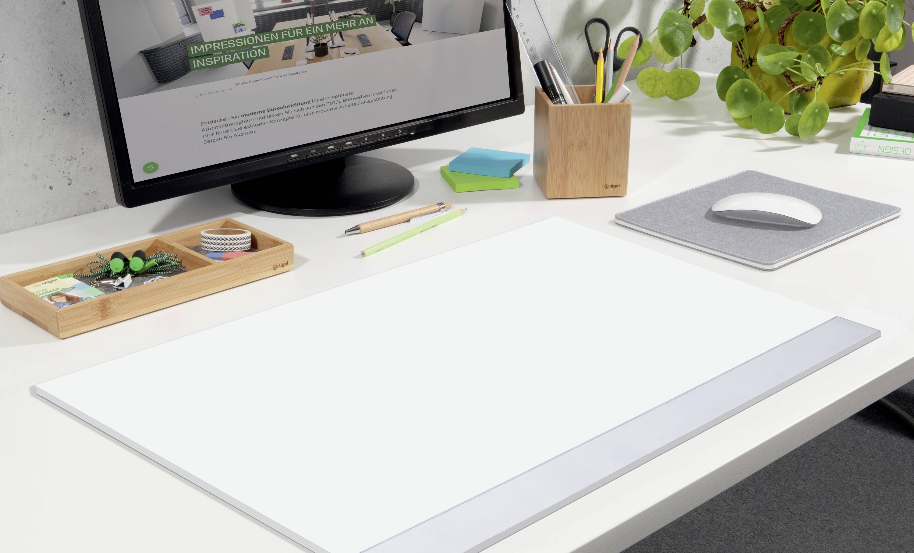 'Modern, opgeruimd kantoor met monitor en toebehoren; focus op witte bureauonderlegger. Planten en schrijfgerei op de achtergrond.'