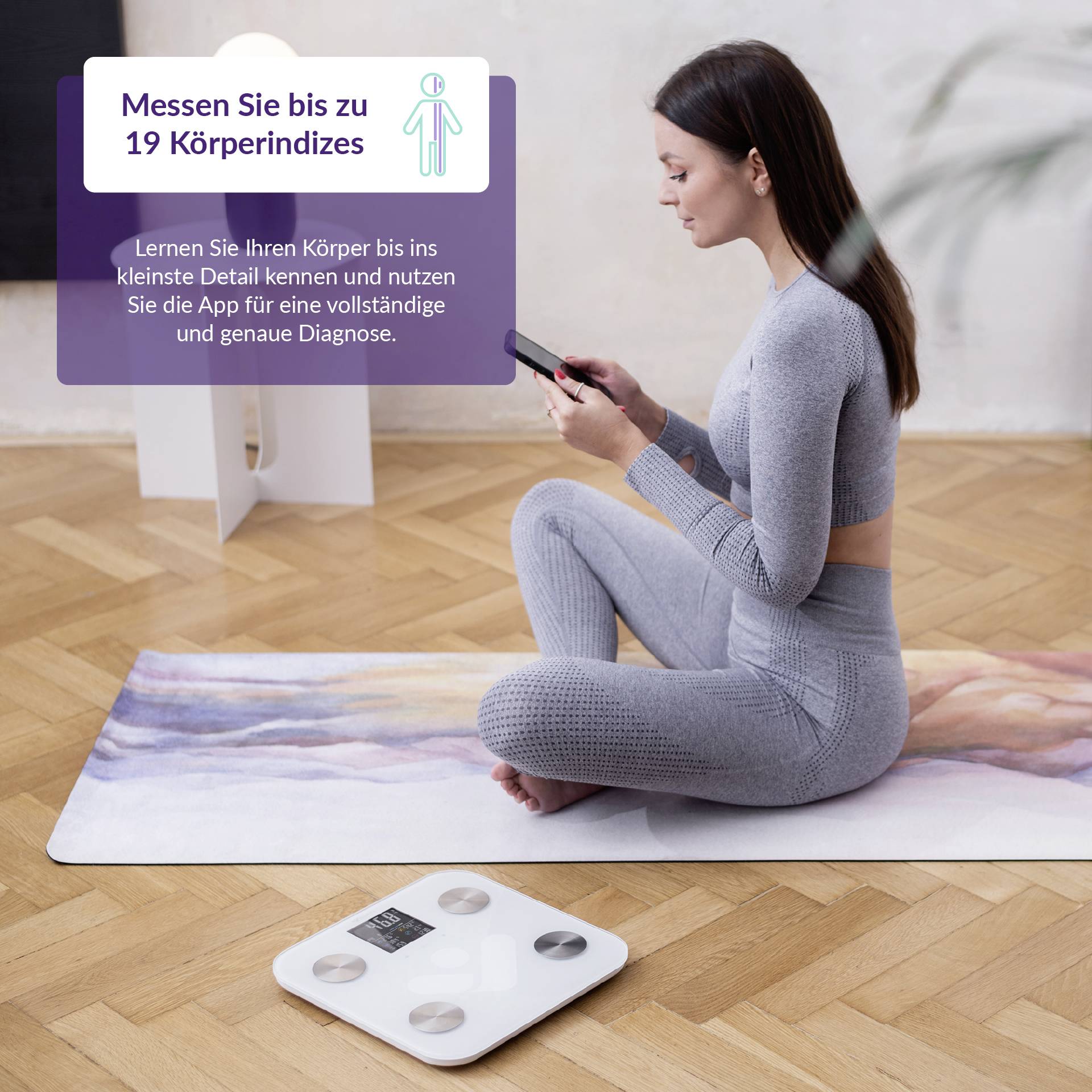 Een vrouw in sportkleding zit op een yogamat en houdt een smartphone vast. Naast haar staat een weegschaal op de vloer.
