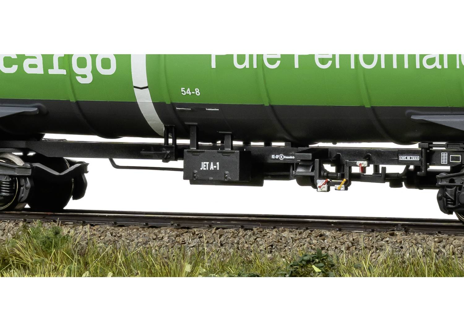 Een groene treinwagon met de opdruk 'JET-A1' op een zwarte doos aan de onderkant, rijdt over sporen langs een met gras begroeid terrein.