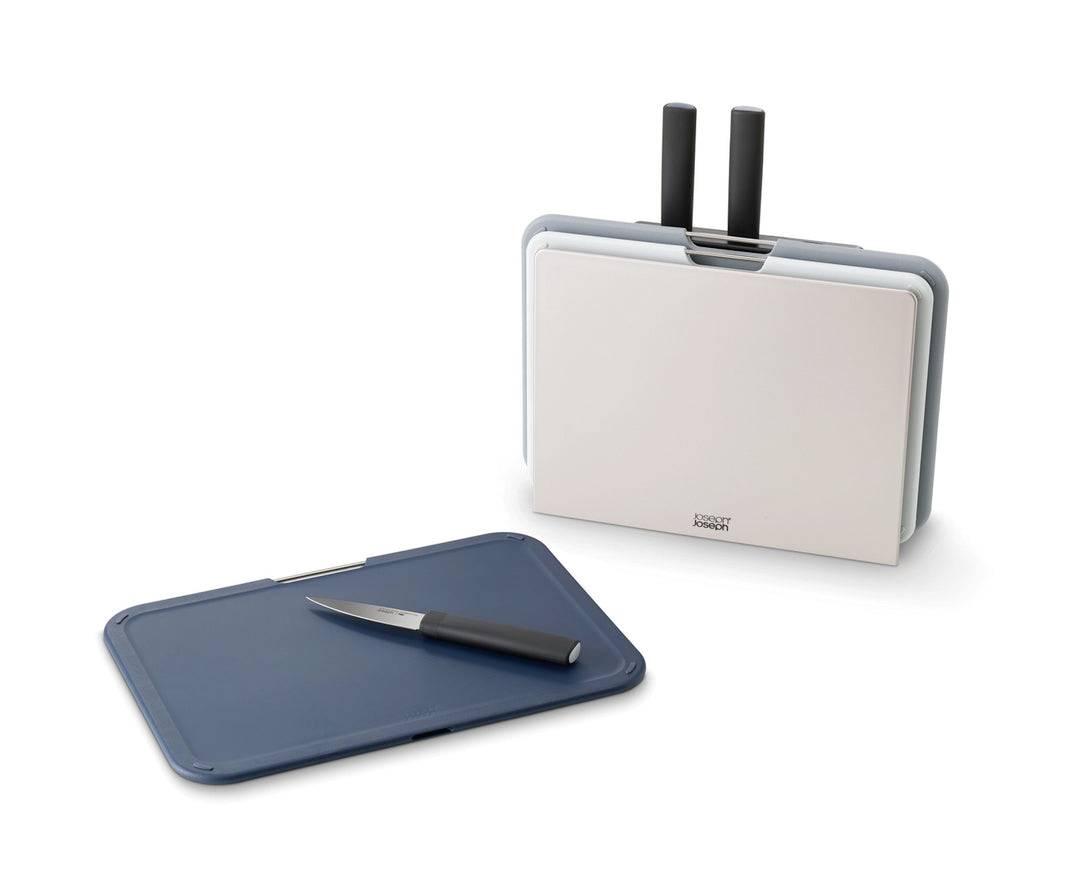 Een mes en een blauw snijplankje liggen naast elkaar, op de achtergrond een messenblok met nog meer messen en snijplanken.