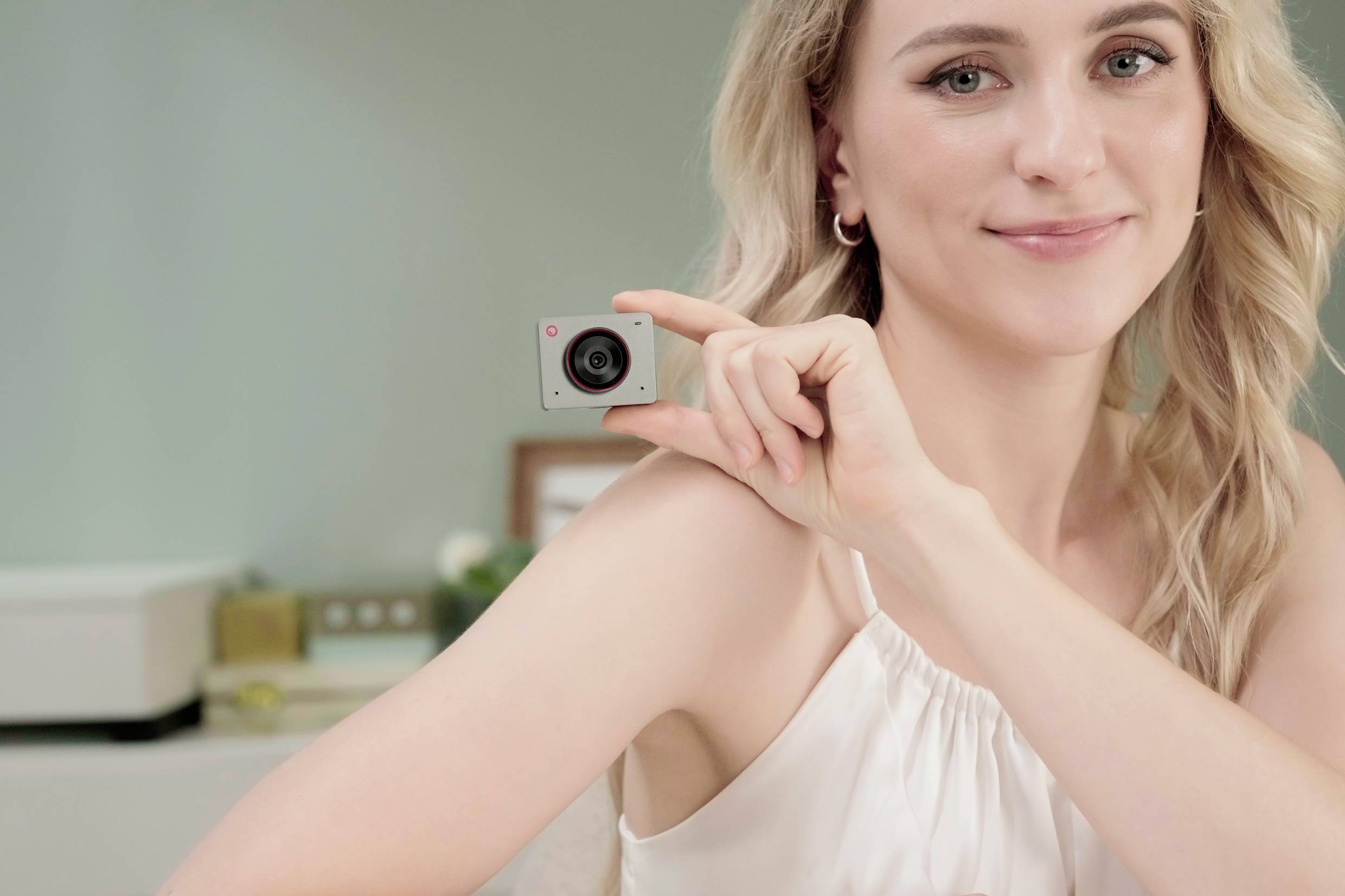 Een vrouw houdt een kleine camera vast en glimlacht, achtergrond wazig.