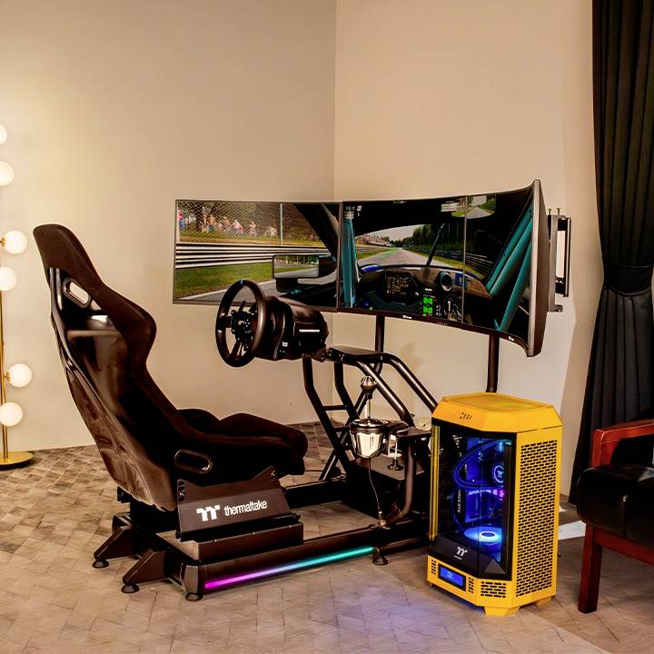 'Een racesimulator met stuur en meerdere monitors, toont een racespel. Op de achtergrond staat een verlichte computer.'