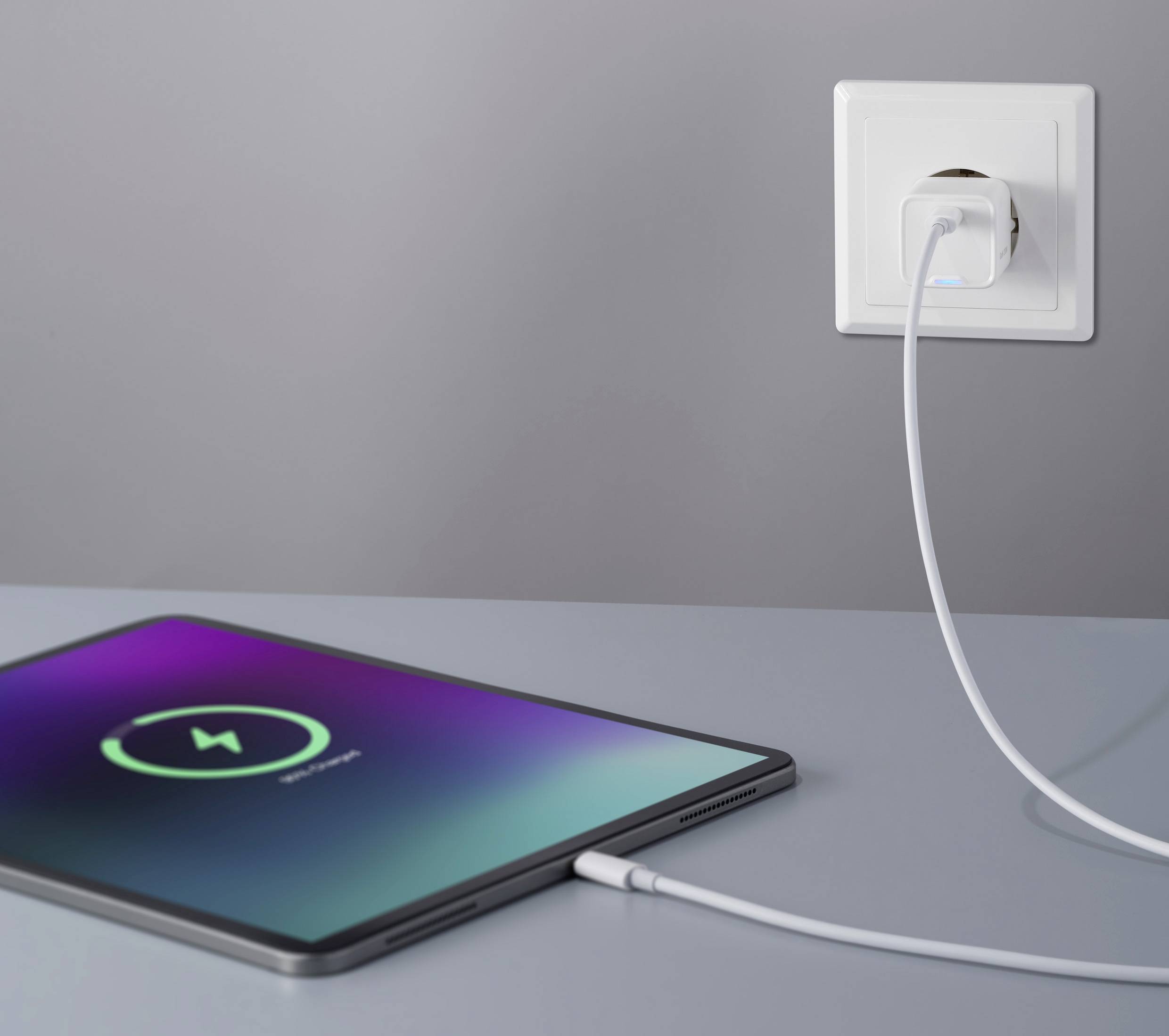 Een tablet ligt op een tafel, verbonden met een oplaadkabel die is aangesloten op een stopcontact. Het scherm toont een oplaadsymbool.