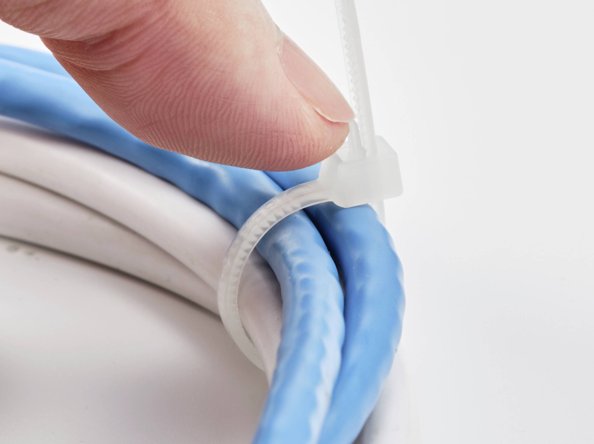 Een hand trekt een kabelbinder strak om blauwe en witte kabels te bundelen.
