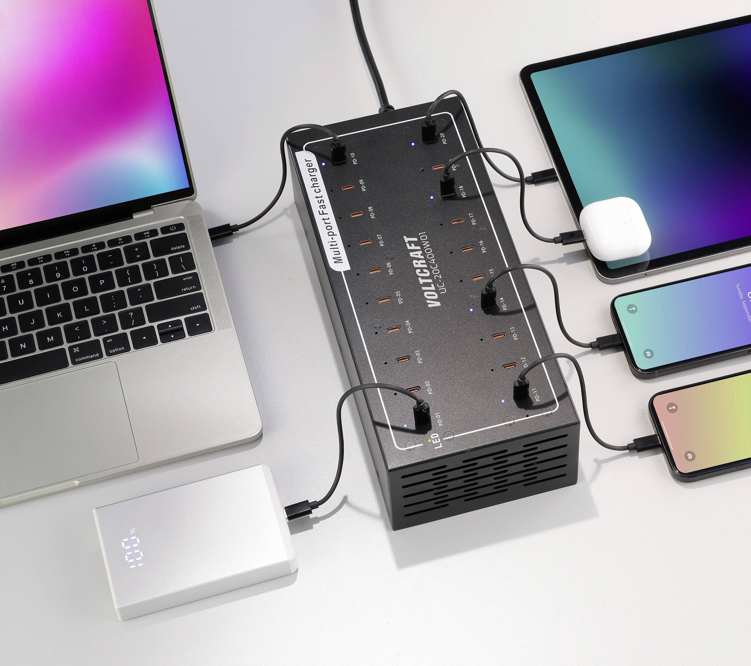 Een multi-USB-oplader laadt gelijktijdig een laptop, een tablet en twee smartphones op. Nog een apparaat is ernaast aangesloten.