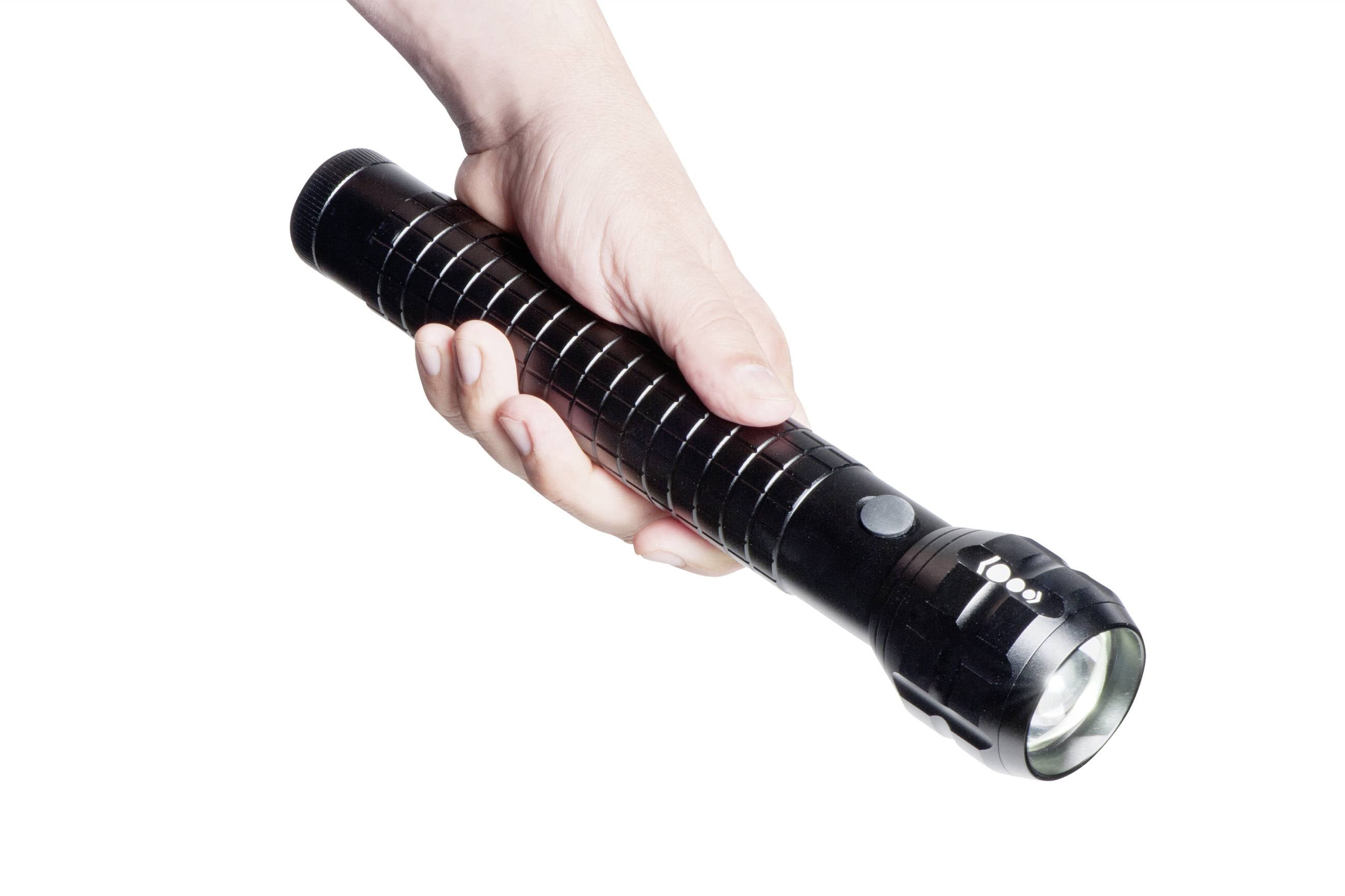 Een rechterhand houdt een zwarte, langwerpige zaklamp vast, die aanstaat en naar beneden schijnt.