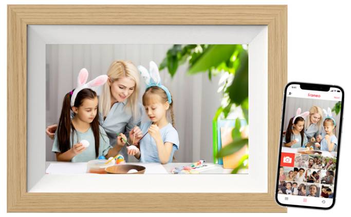 Een vrouw en twee kinderen met konijneoren beschilderen eieren. Op de voorgrond toont een mobiele telefoonscherm dezelfde foto in een app.