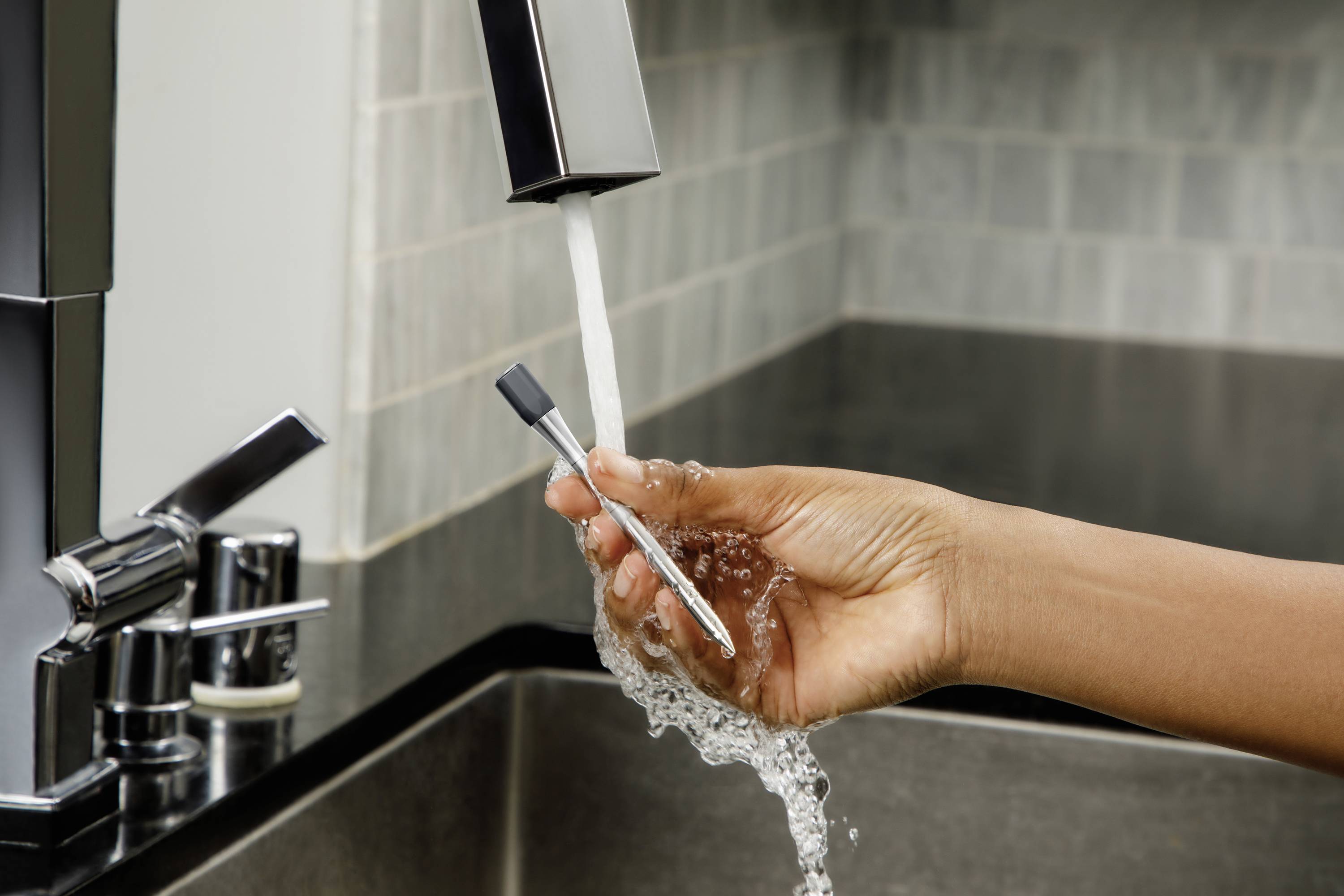 Een hand houdt een scheerapparaat onder stromend water bij een wastafel om het te reinigen.