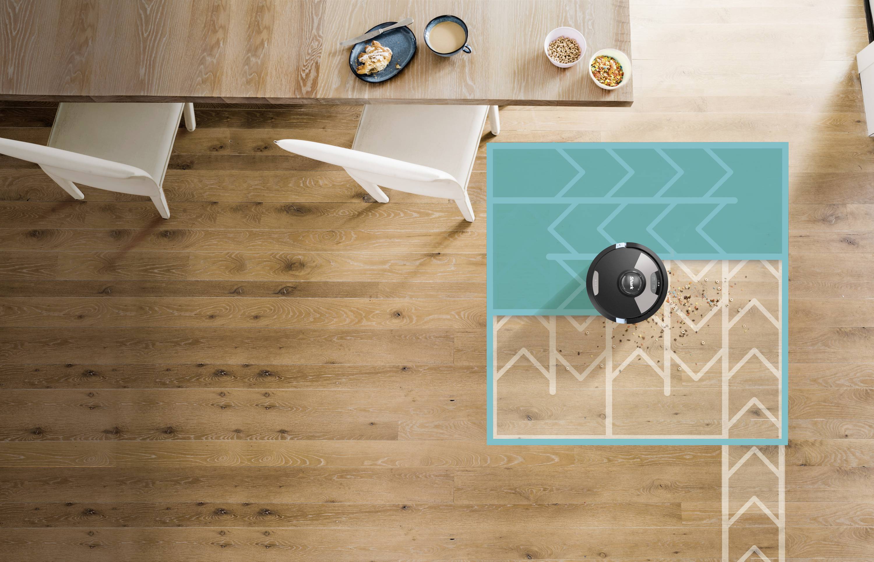 Een robotstofzuiger reinigt een houten vloer naast een eettafel met twee lichte stoelen en servies erop.