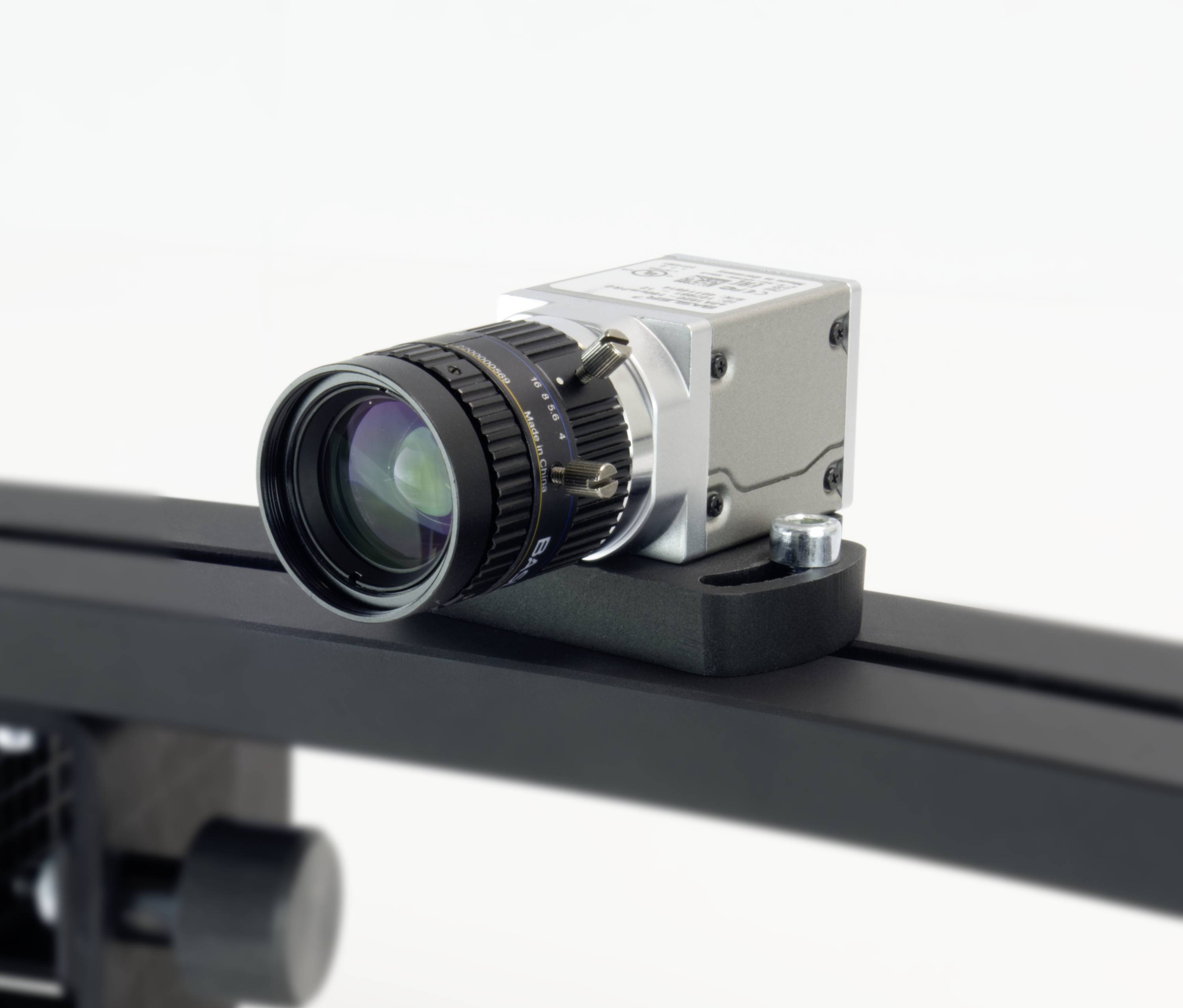 Een camera met een lens is gemonteerd op een zwarte houder, mogelijk onderdeel van een bewakingssysteem of productielijn.