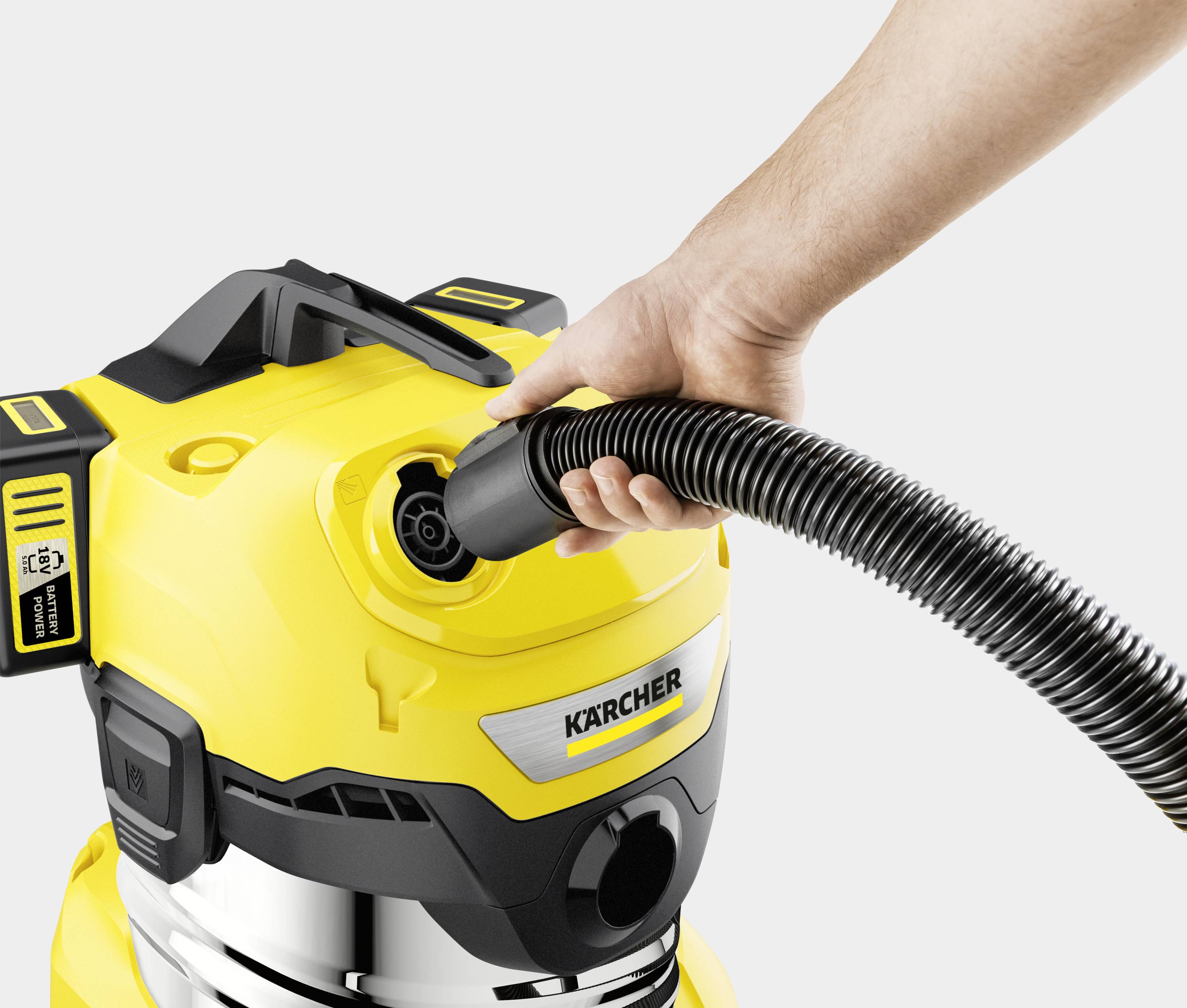 Een hand steekt een slang in een gele stofzuiger. De stofzuiger heeft zilveren en zwarte details en het logo 'Kärcher'.