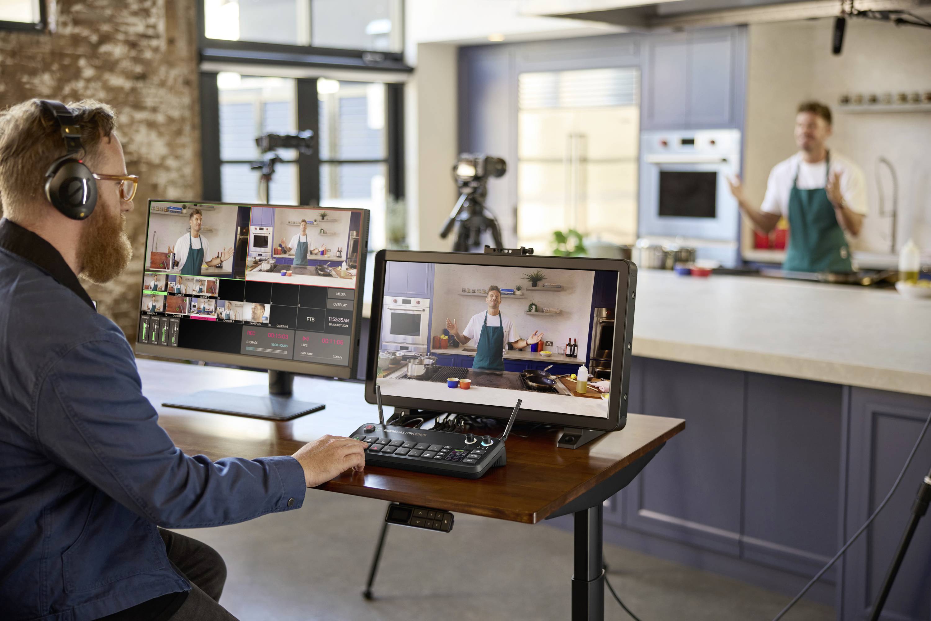 Een man met koptelefoon zit aan een bureau met computers en videoapparatuur, terwijl een kok op de achtergrond filmt.
