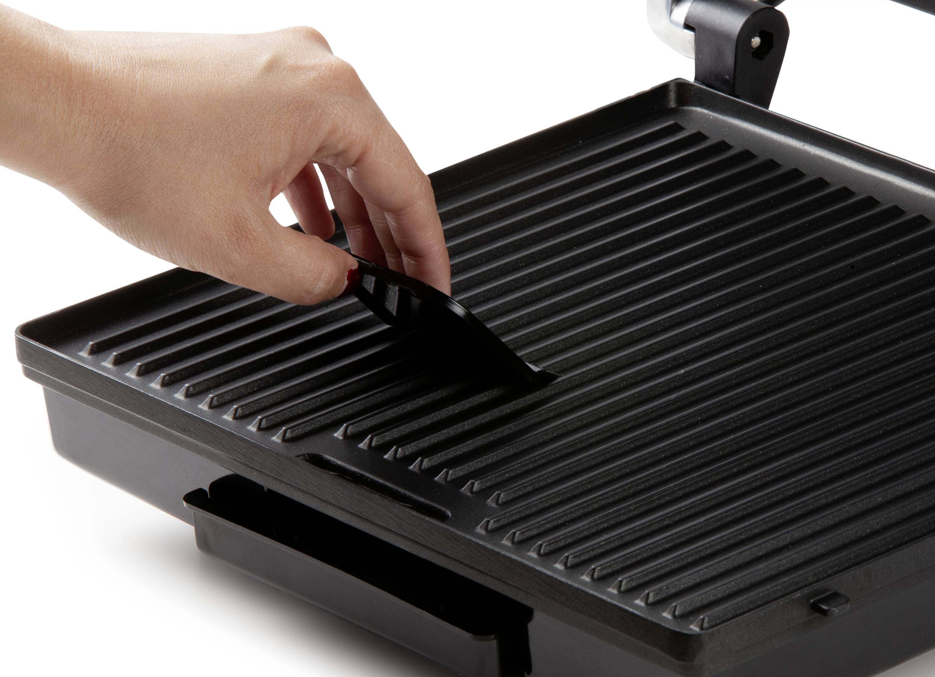 Een hand tilt het rooster van een contactgrill op. De grill heeft een geribde oppervlakte, geschikt voor het bakken van vlees of groenten.