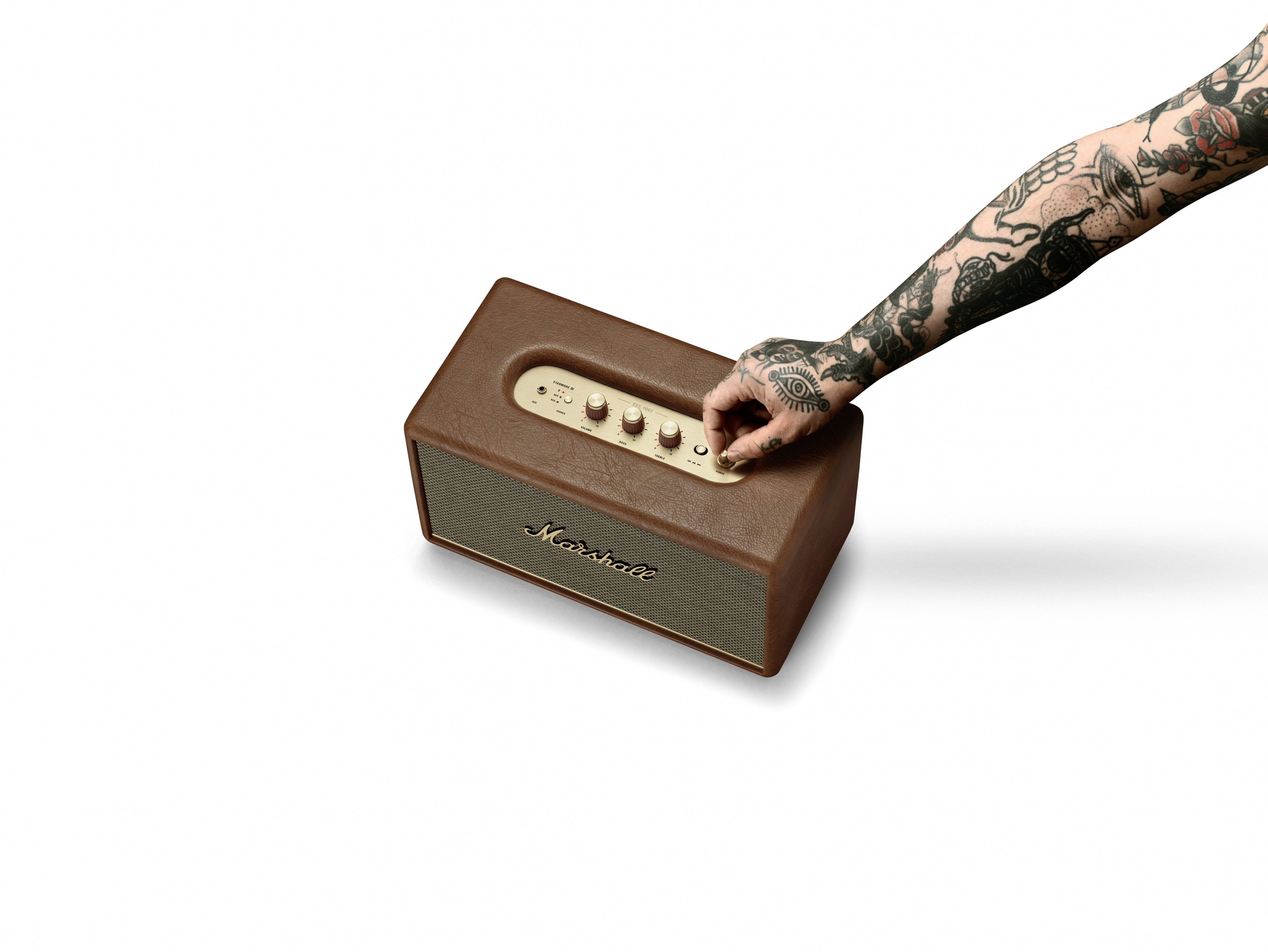 Een getatoeëerde hand stelt het volume in op een bruine luidspreker waarop 'Marshall' staat.