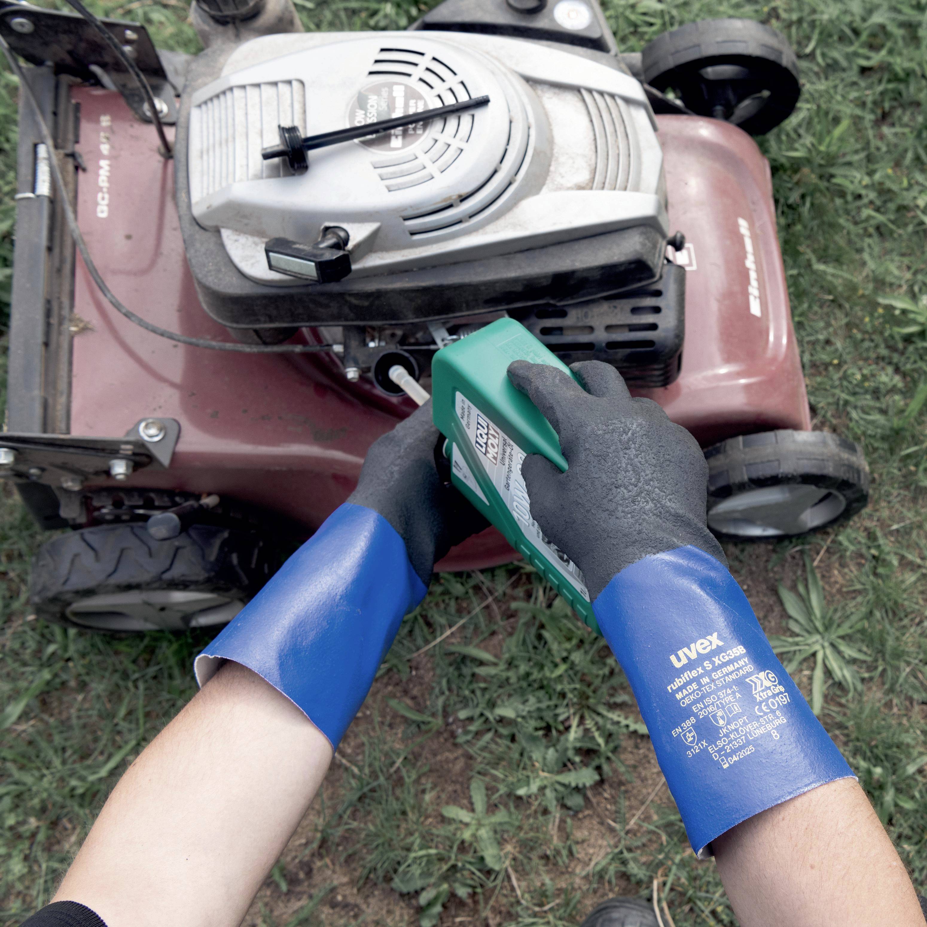 Een persoon vult benzine in een grasmaaier. Ze draagt blauwe beschermende handschoenen. De grasmaaier staat op een grasveld.