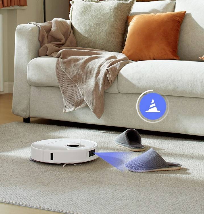 Een robotstofzuiger navigeert om pantoffels voor een bank. Een lichtsignaal toont zijn reinigings- en hindernismijdende capaciteiten.