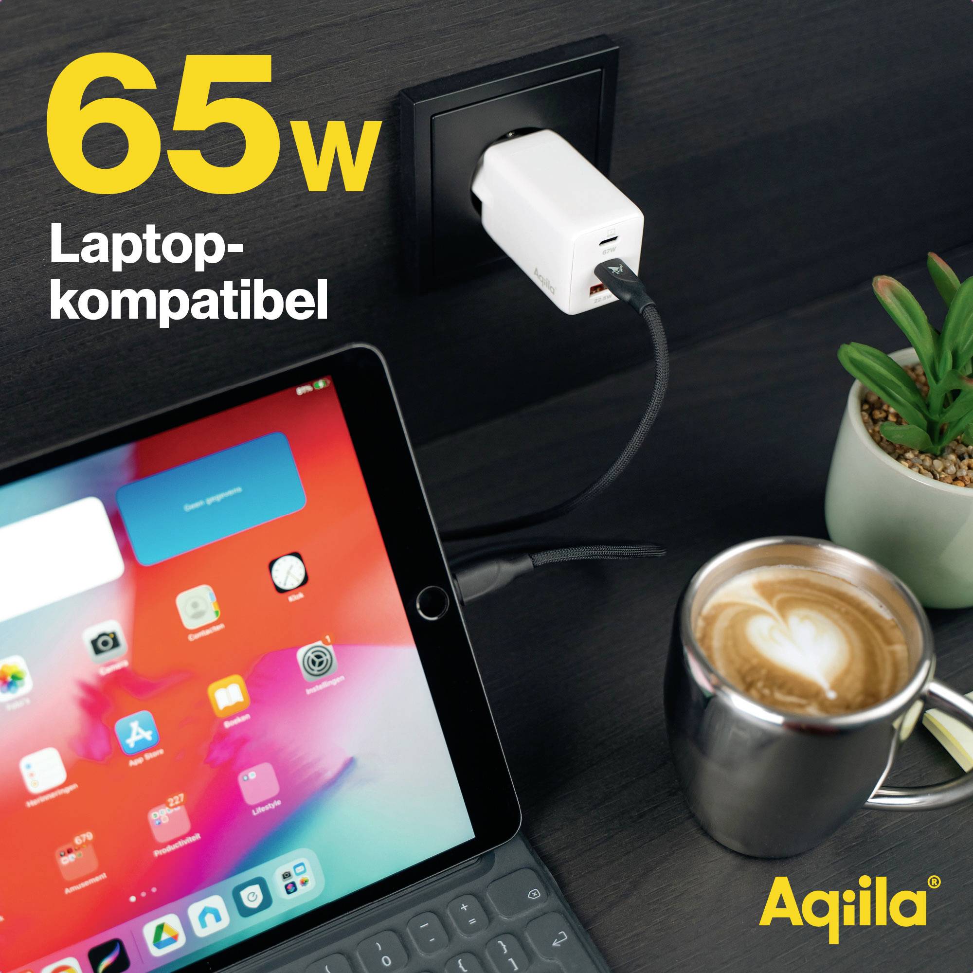 Een oplader steekt in het stopcontact met de tekst '65W laptop-compatibel'. Ernaast een tablet, een cappuccino en een plant.