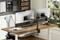 Een bureau met twee monitoren op steunen, een toetsenbord, muis en een laptopstandaard. Op de achtergrond een raam met zicht naar buiten.