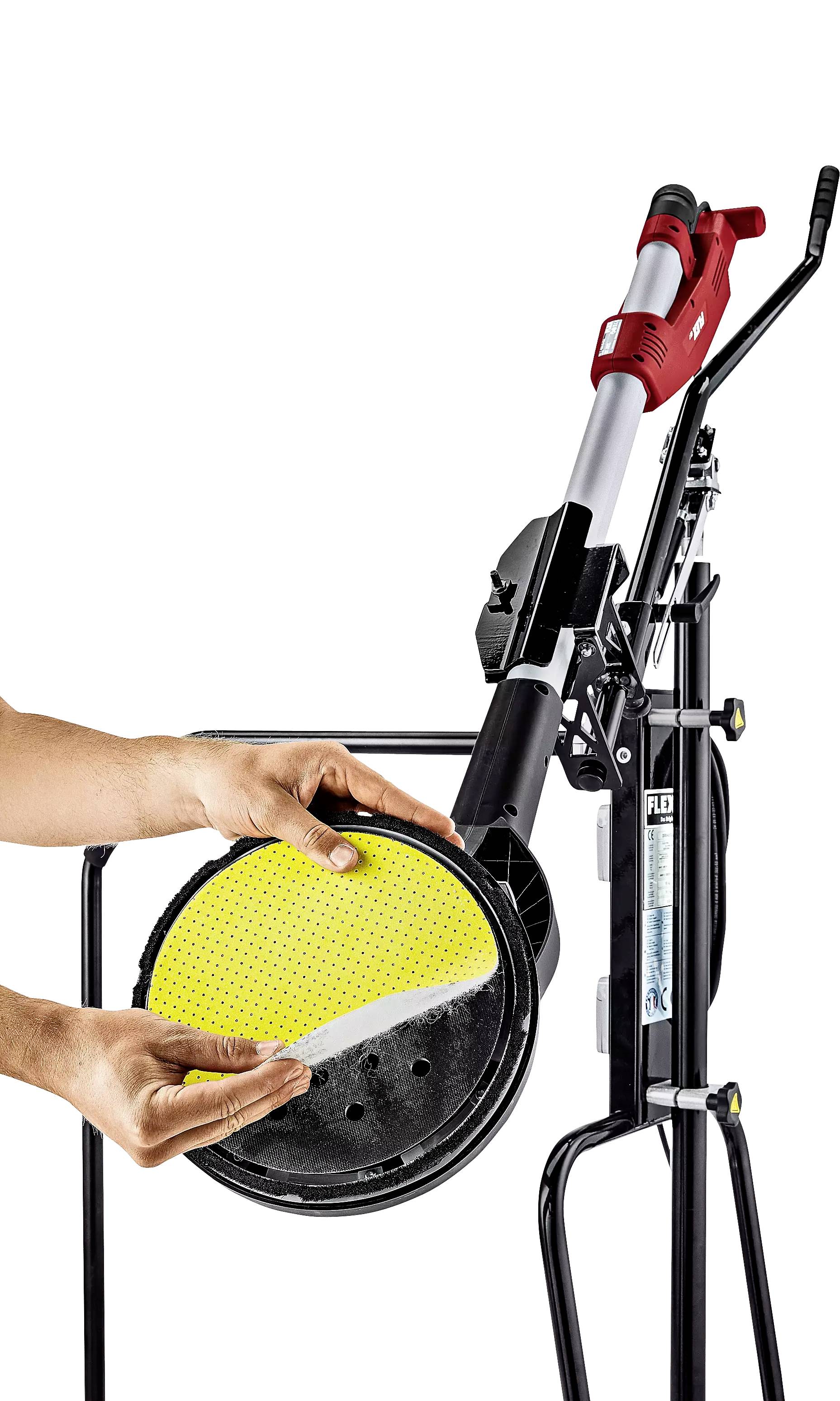 Een persoon bevestigt een gele schuurpad aan een slijpmachine. De machine heeft een rode handgreep en staat gemonteerd op een standaard.