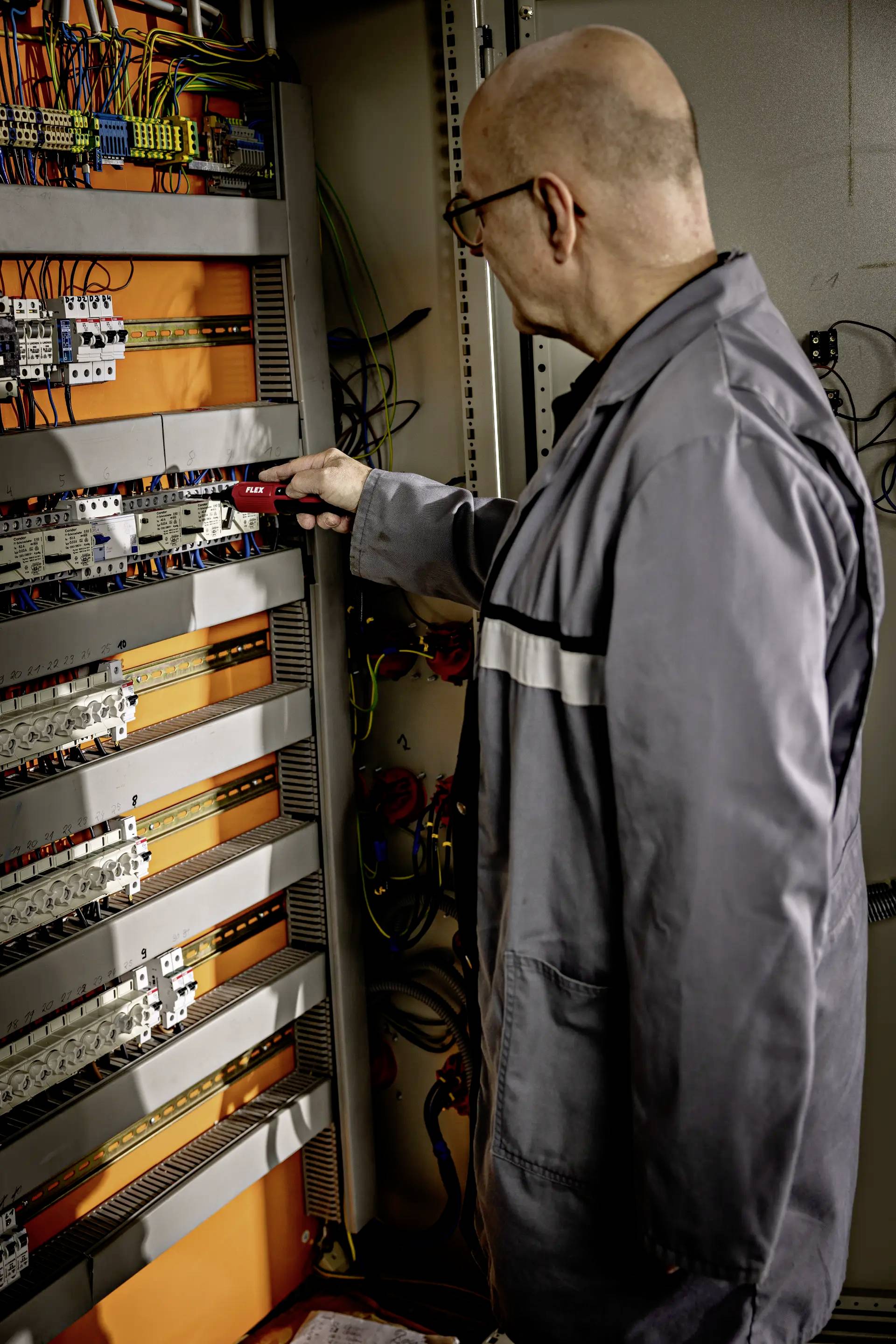Een man in werkkleding controleert schakelingen in een open schakelkast.