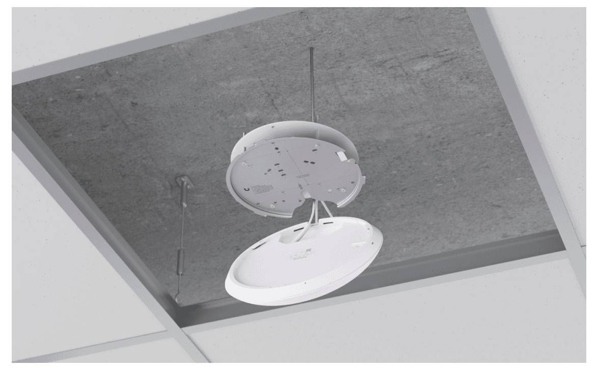 Plafondmontage van een rond, wit apparaat in een open plafond-element, met zichtbare kabels en bevestigingselementen.