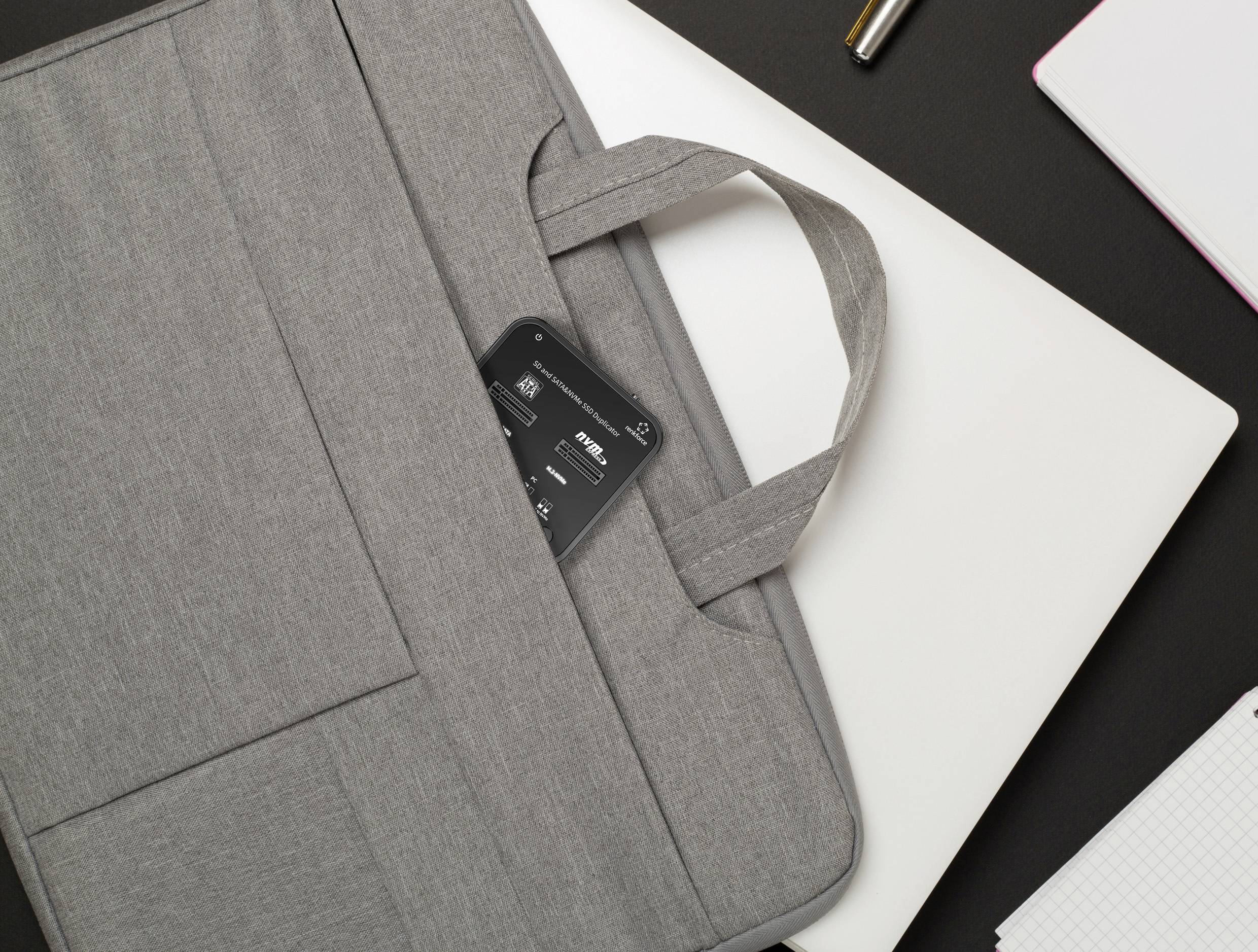 Grijze laptoptas op een tafel, half open met een mobiele telefoon zichtbaar in de tas, omgeven door een witte laptop en schrijfbenodigdheden.