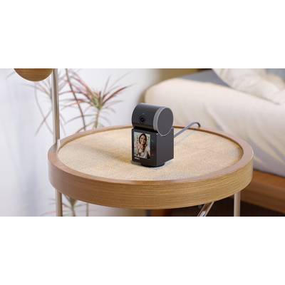 Een slimme camera staat op een rond houten tafelblad. Op haar scherm is het beeld van een persoon tijdens een videogesprek zichtbaar.