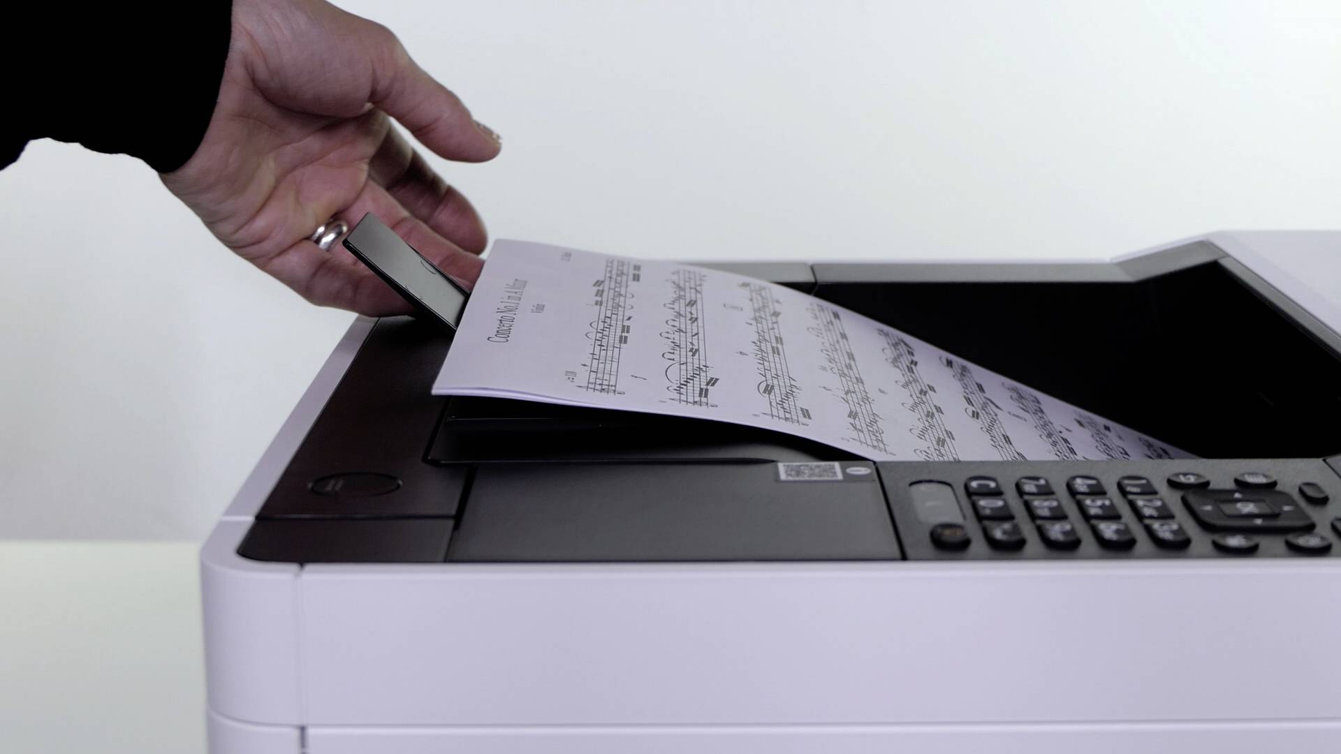 Een hand houdt een USB-stick boven een printer, terwijl een vel met muzieknoten uit de printer steekt.