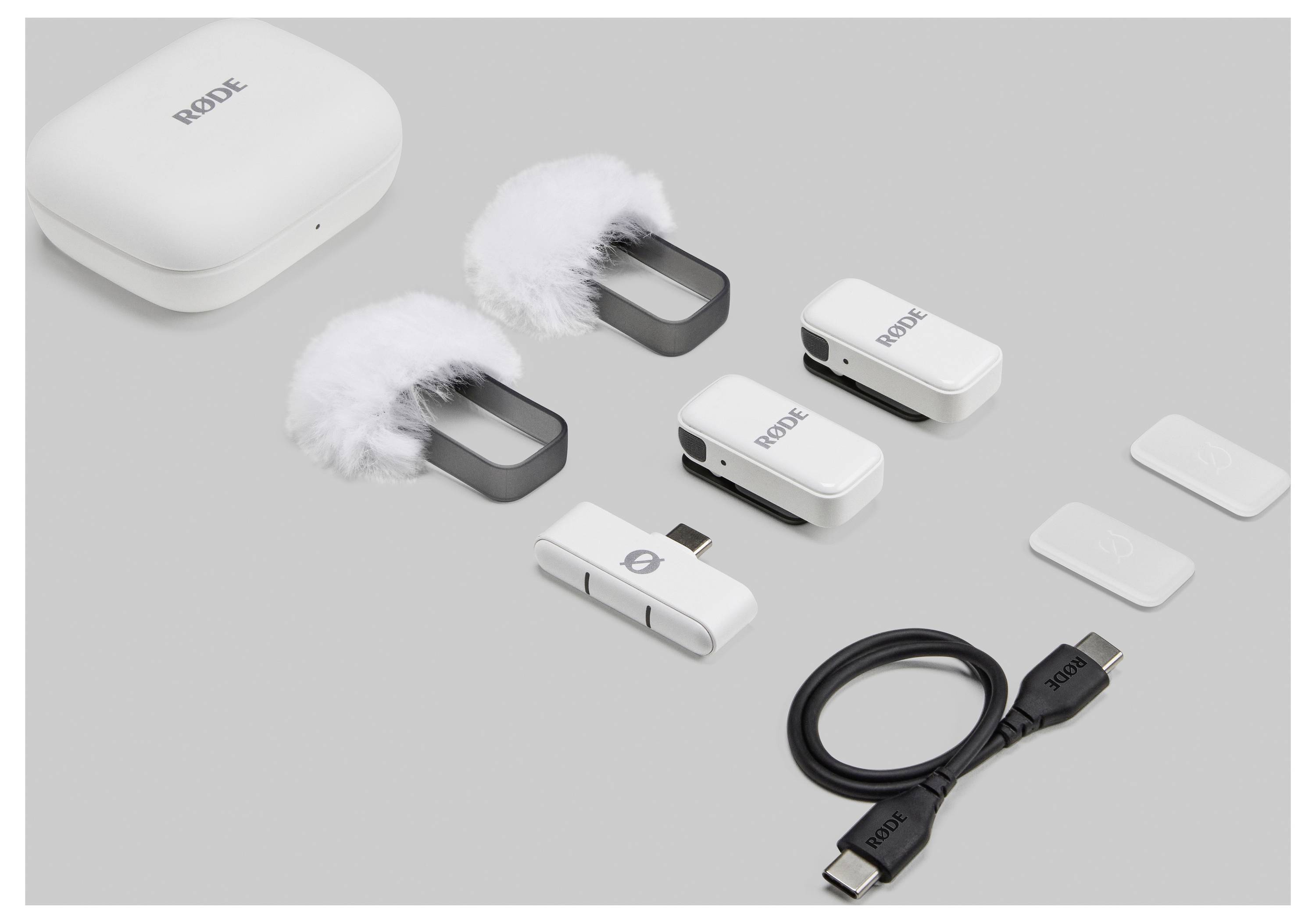 Draadloze microfonenset bestaande uit twee dasspeldmicrofoons met windkap, ontvanger, USB-C-kabel en beschermhoes, op grijze achtergrond.