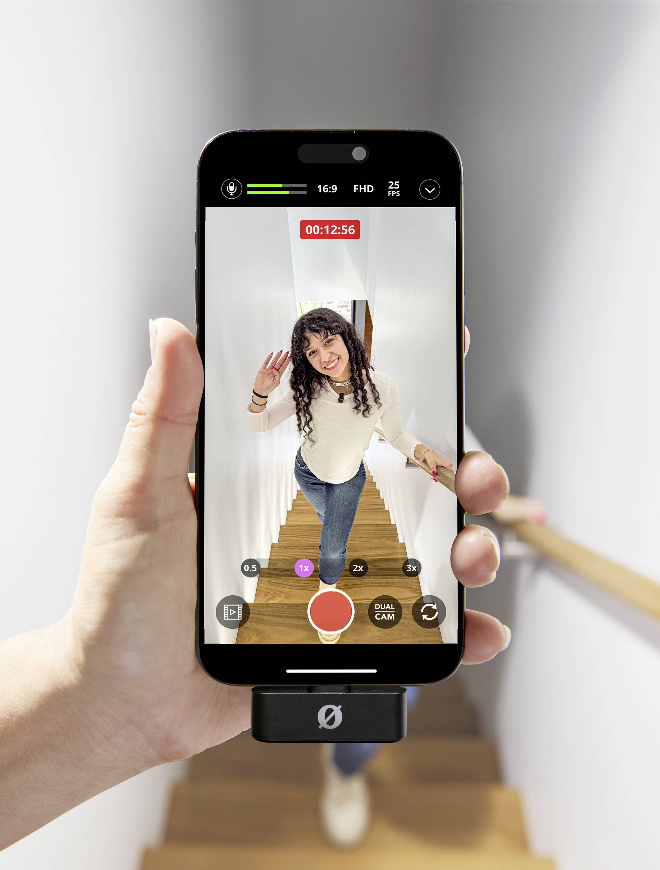 Een persoon staat op een trap en zwaait naar de camera van een smartphone die in de hand wordt vastgehouden. Op het scherm speelt een video-opname.