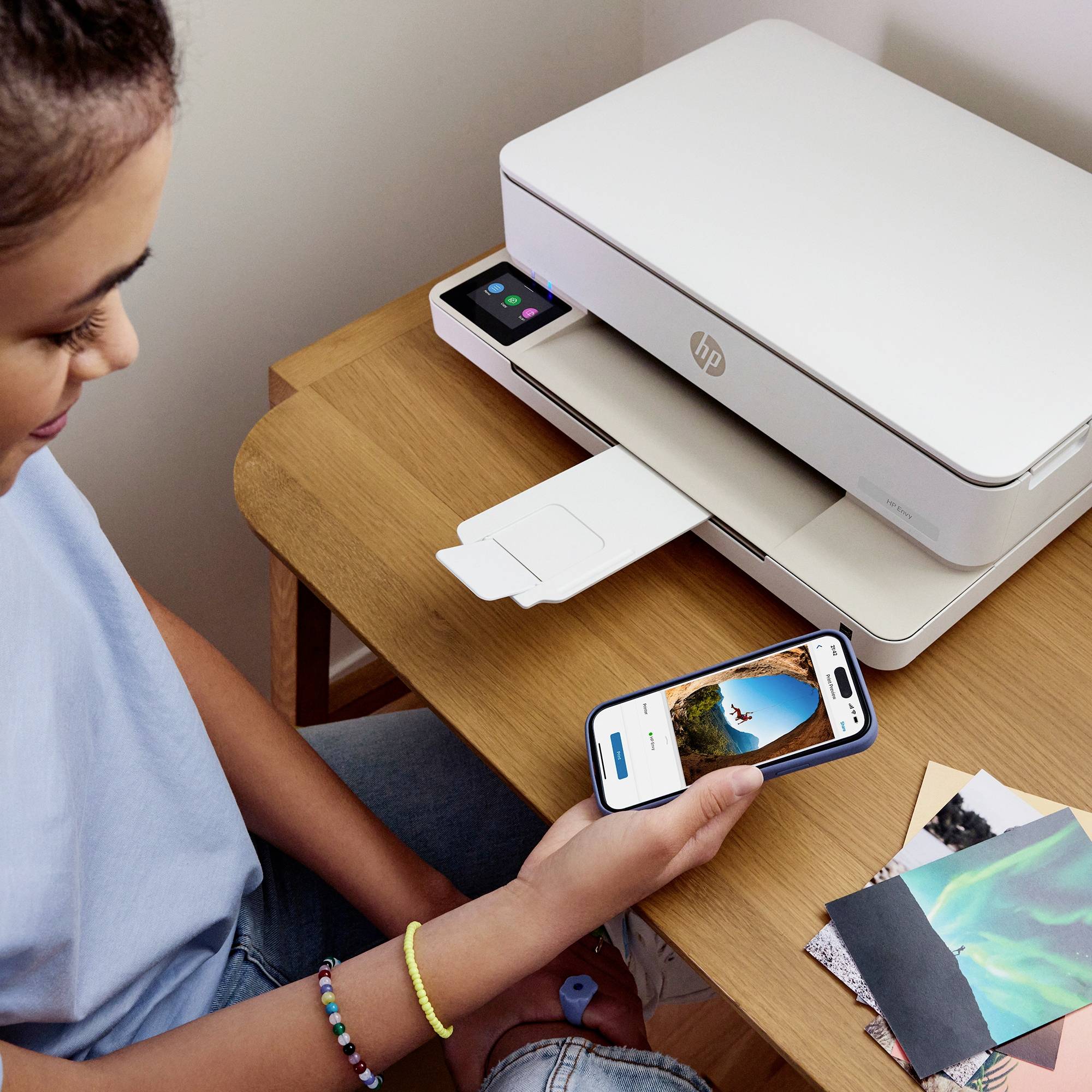 Een persoon gebruikt een smartphone om een foto rechtstreeks naar een printer te sturen. De printer staat op een houten tafel.