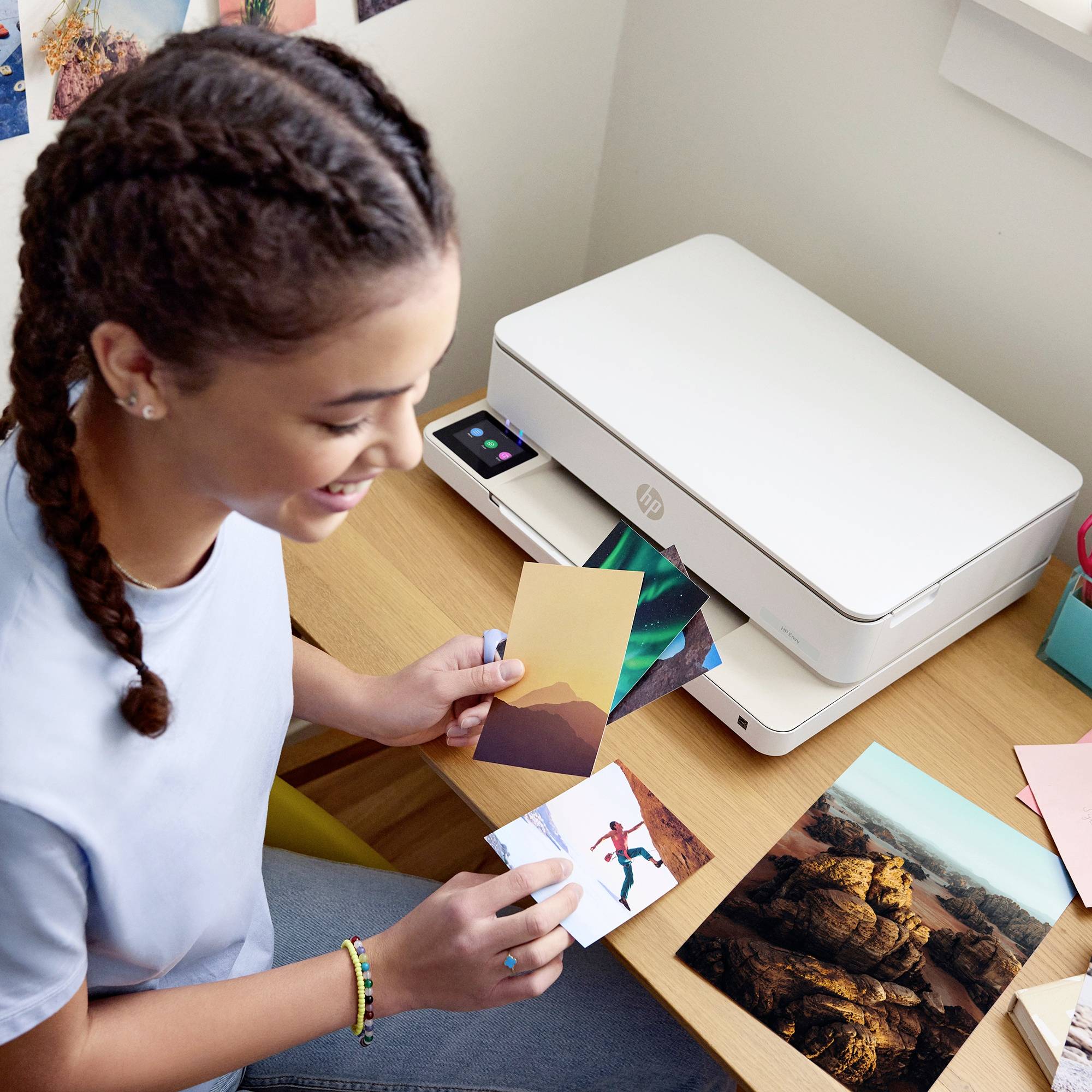 Een persoon met gevlochten haar glimlacht terwijl ze foto's naast een printer sorteert. Op de achtergrond zijn meer foto's zichtbaar.