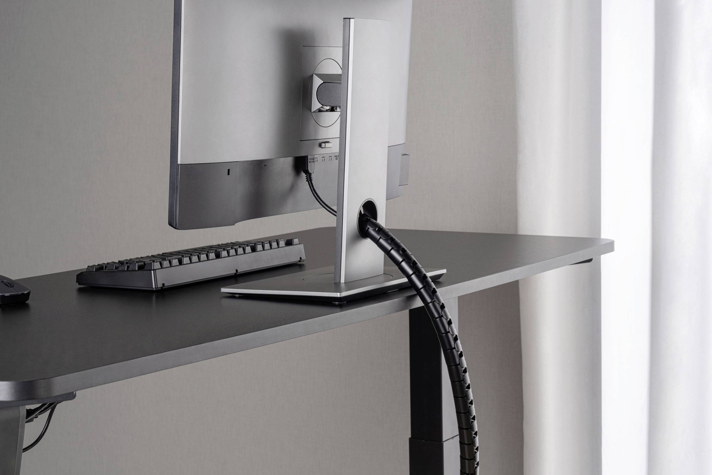 Computerscherm en toetsenbord op een zwart bureau, kabelbeheer door de monitorstandaard.