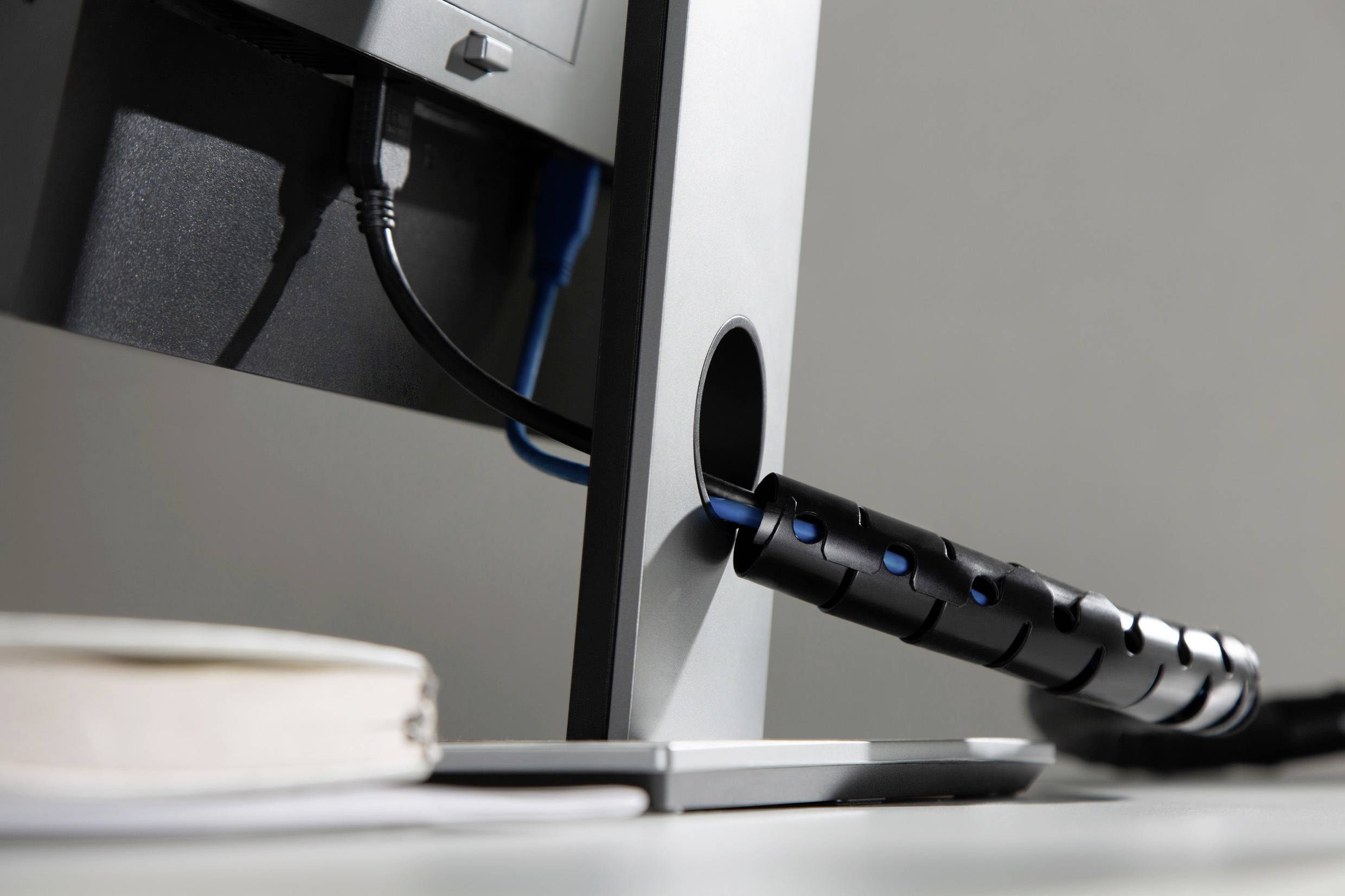Een computermonitor met kabelbeheer bij de kabeluitgang. Op de voorgrond is een notitieboek onscherp zichtbaar.