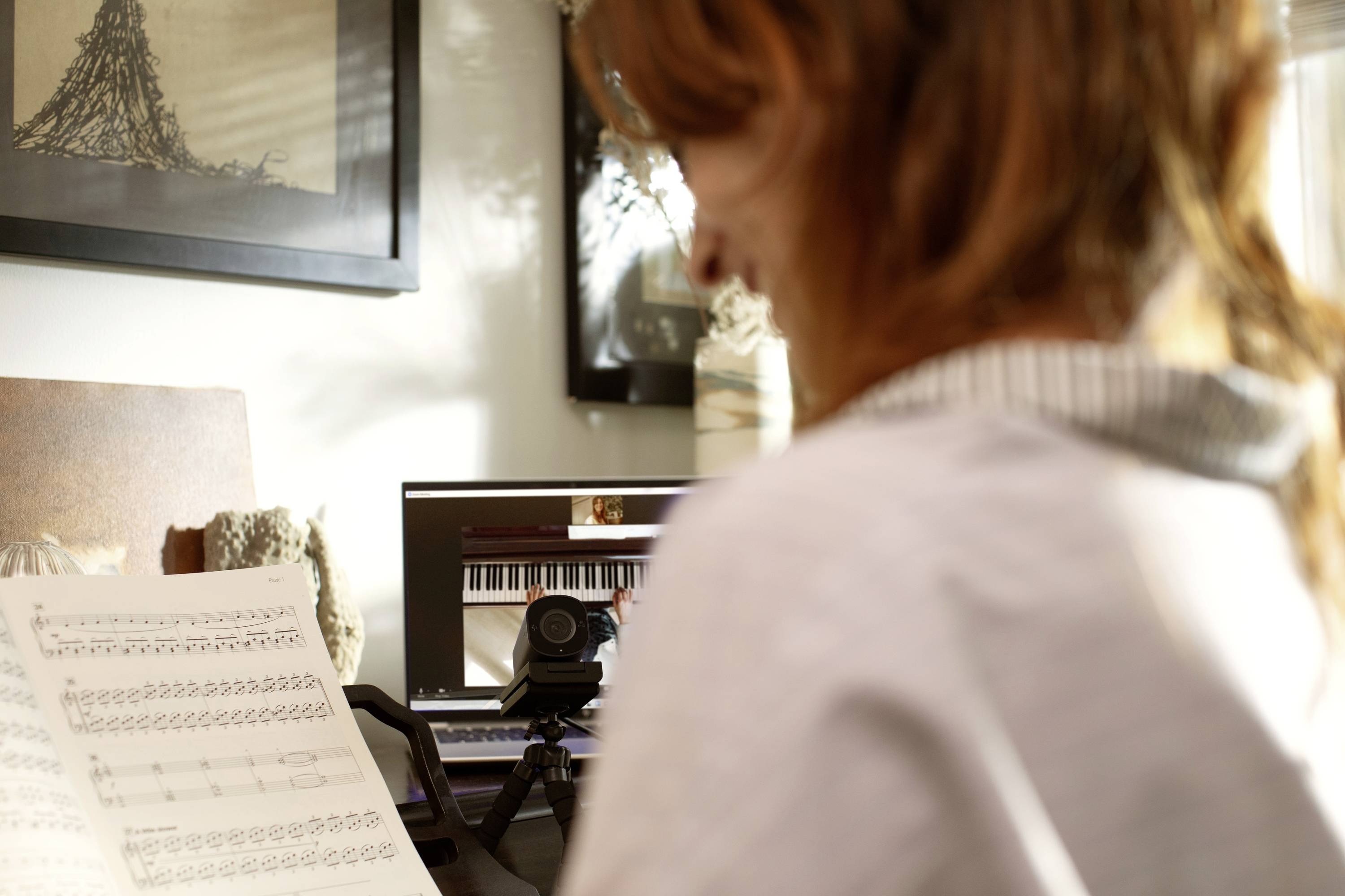 Een persoon kijkt naar een muziekpartituur voor een laptop met een afbeelding van een piano op het scherm. Naast de laptop staat een camera.