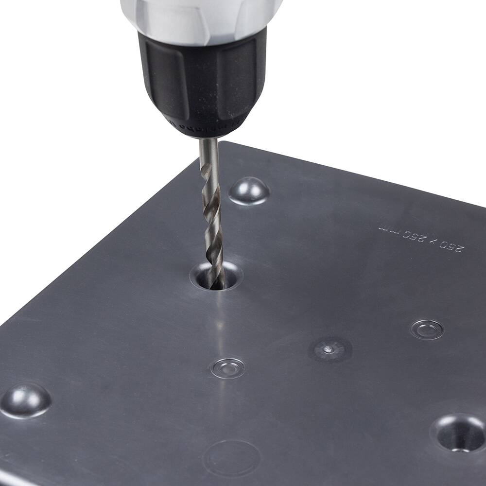 Een boormachine boort een gat in een metalen plaat. De boor is in actie, en er zijn meerdere voorgeboorde gaten in de plaat.