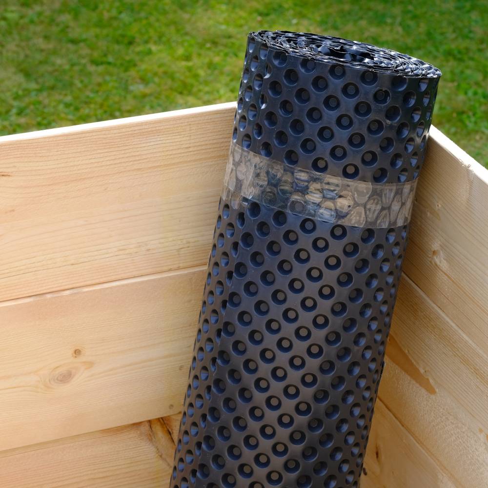 Een zwarte nokkenmat staat rechtop in een houten kist buiten. De mat is geschikt voor bescherming of drainage.