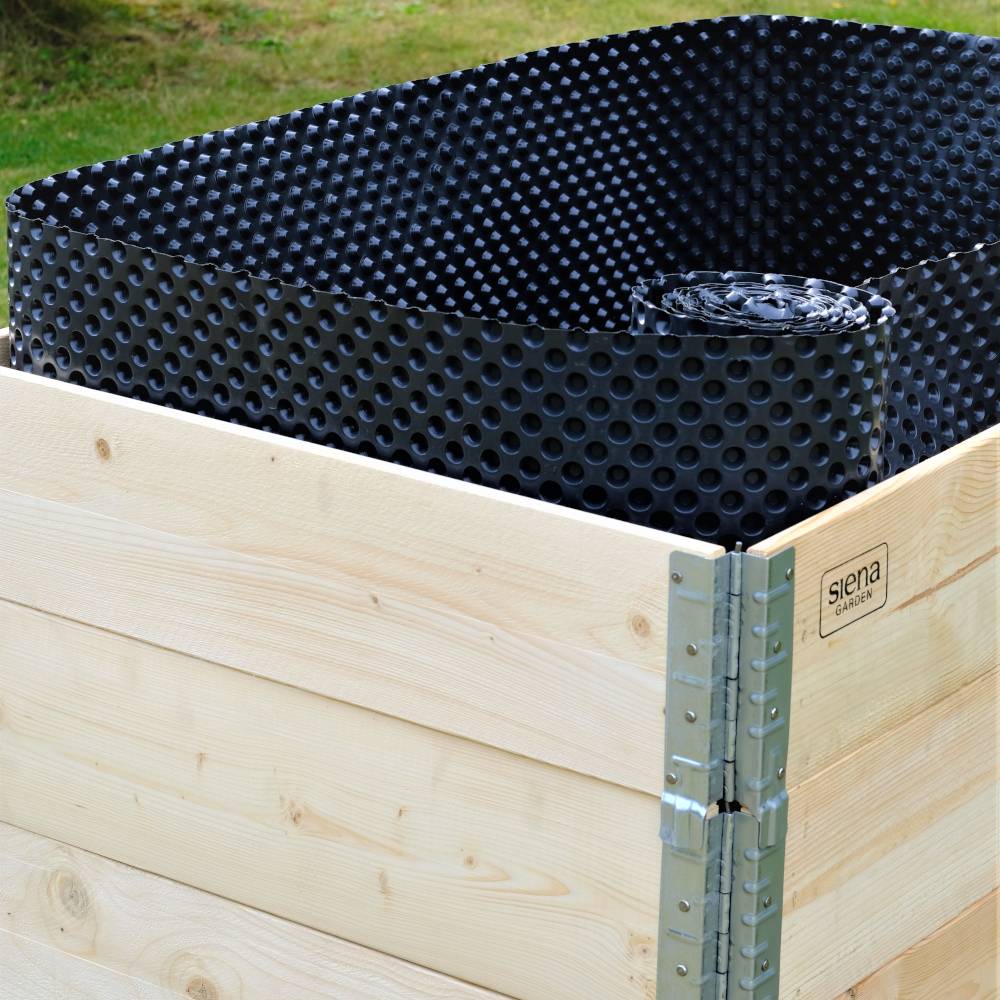 Een houten kist bevat een opgerolde, zwarte noppen-folie. De kist staat buiten op een weiland.
