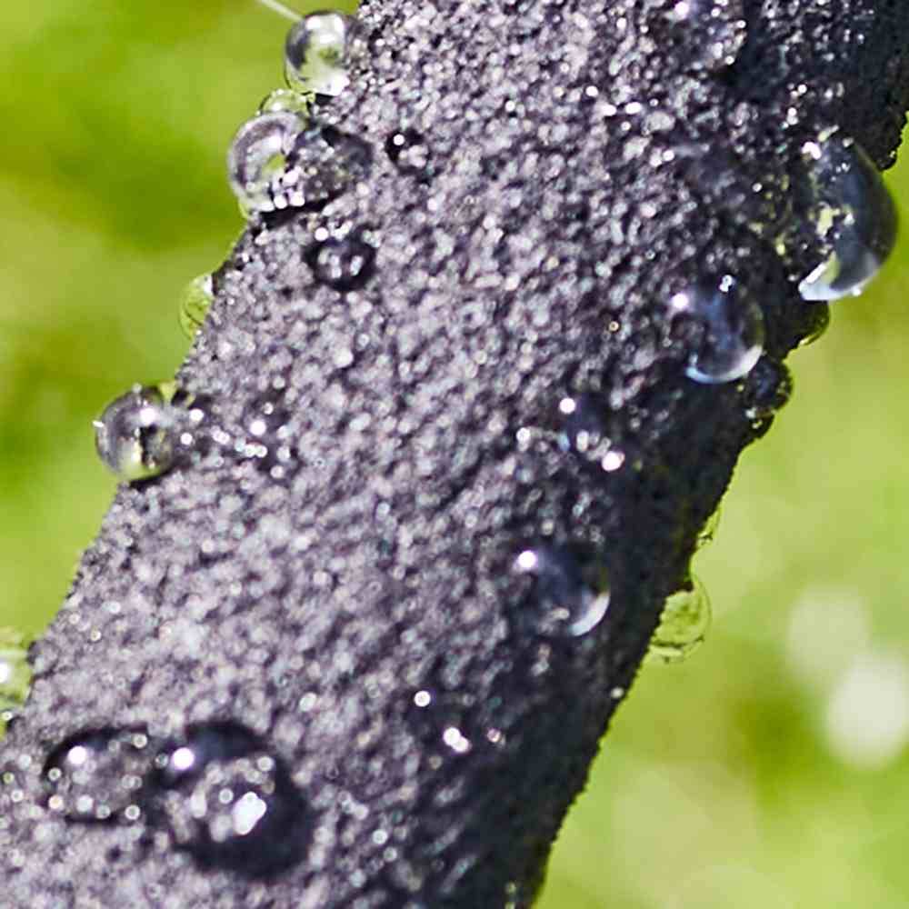 Waterdruppels op een donkere, gestructureerde tak van dichtbij, omgeven door een groene achtergrond.