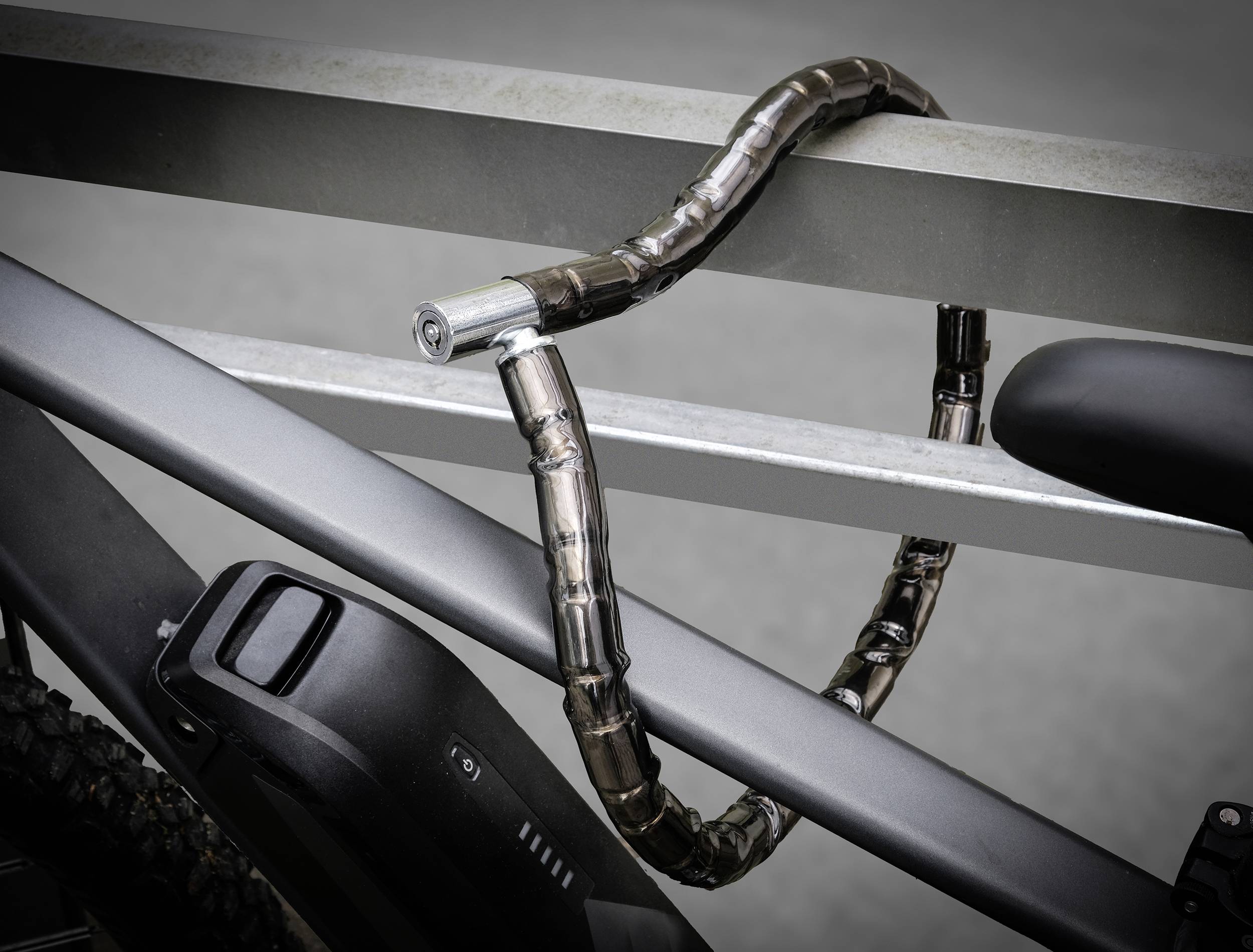 Een zwarte fiets is met een robuust metalen slot vastgemaakt aan een grijs metalen hek.