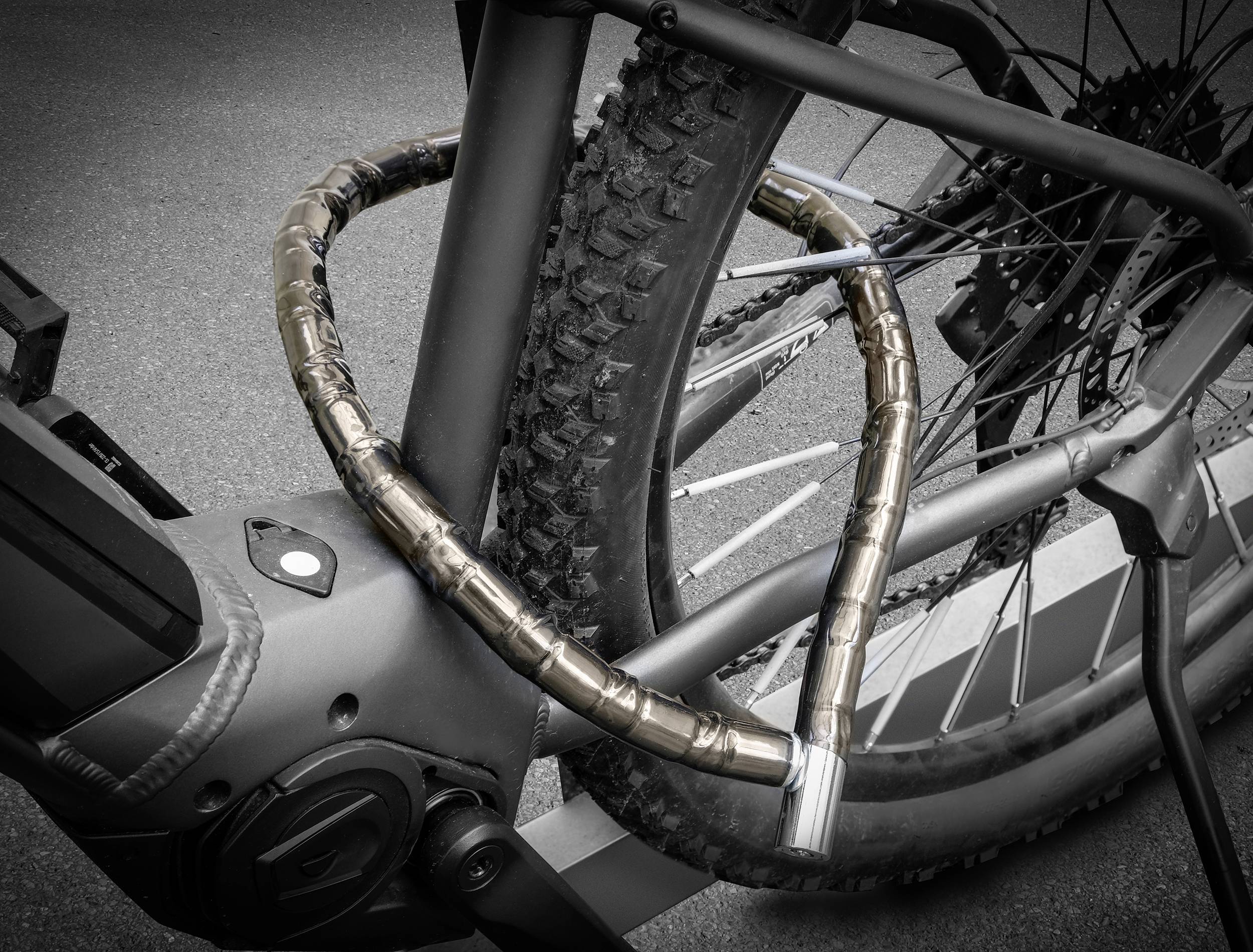 Een fiets is met een stevig, gecamoufleerd kettingslot aan een achterwiel bevestigd. De fiets staat op een geaspfalteerde ondergrond.