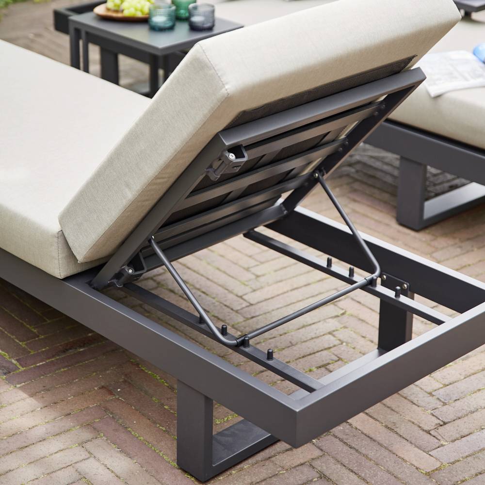 Ligstoel met verstelbare rugleuning op een terras van houten planken. Op de achtergrond een tafel met decoratie.