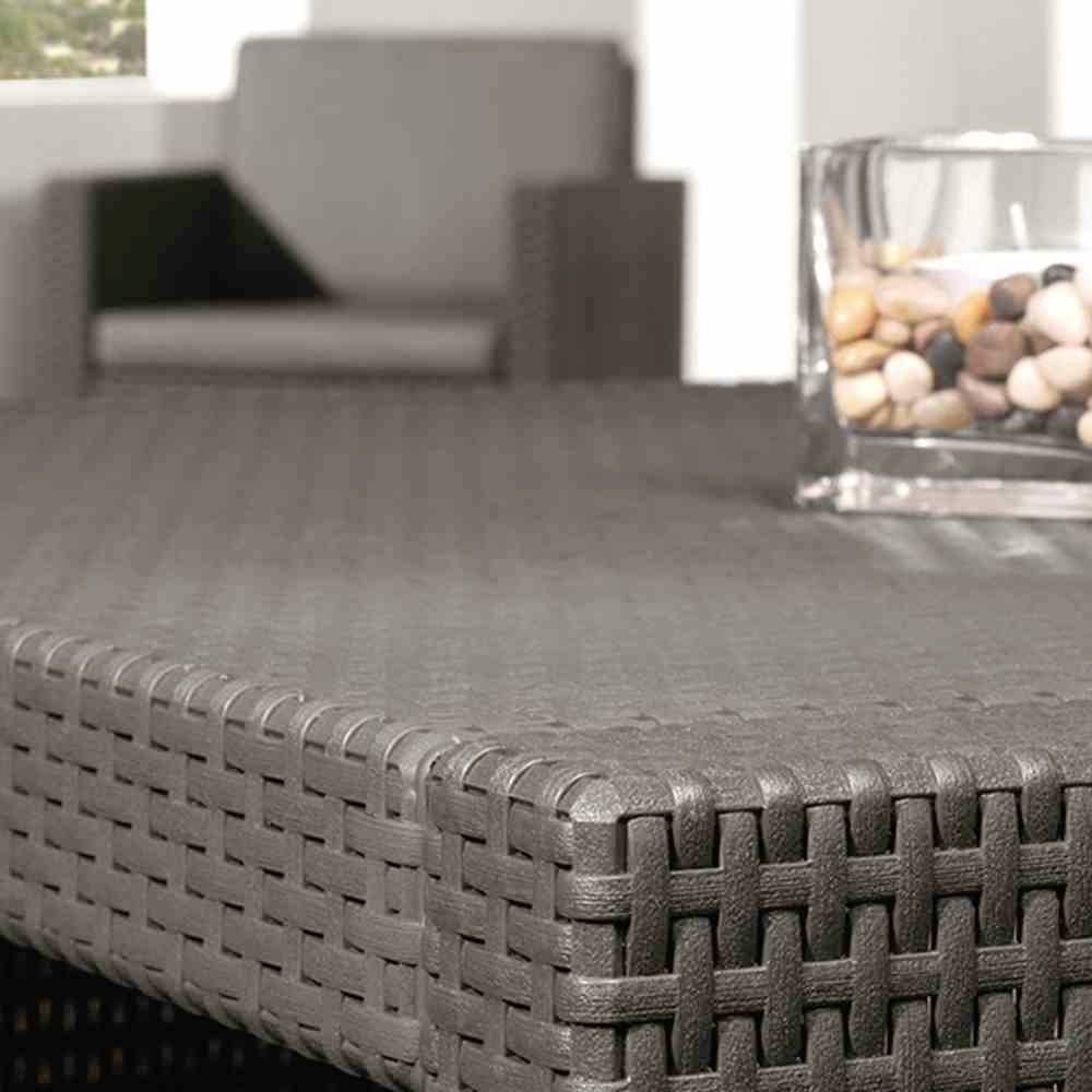 Een gevlochten tafel met een glazen vaas vol kiezels erop, een onscherpe stoel op de achtergrond.