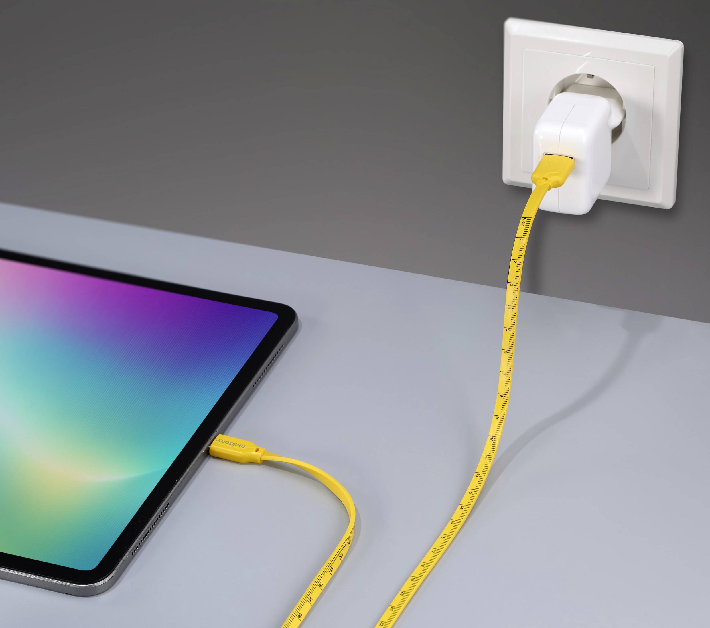 Tablet op tafel met geel oplaadkabel in stopcontact.