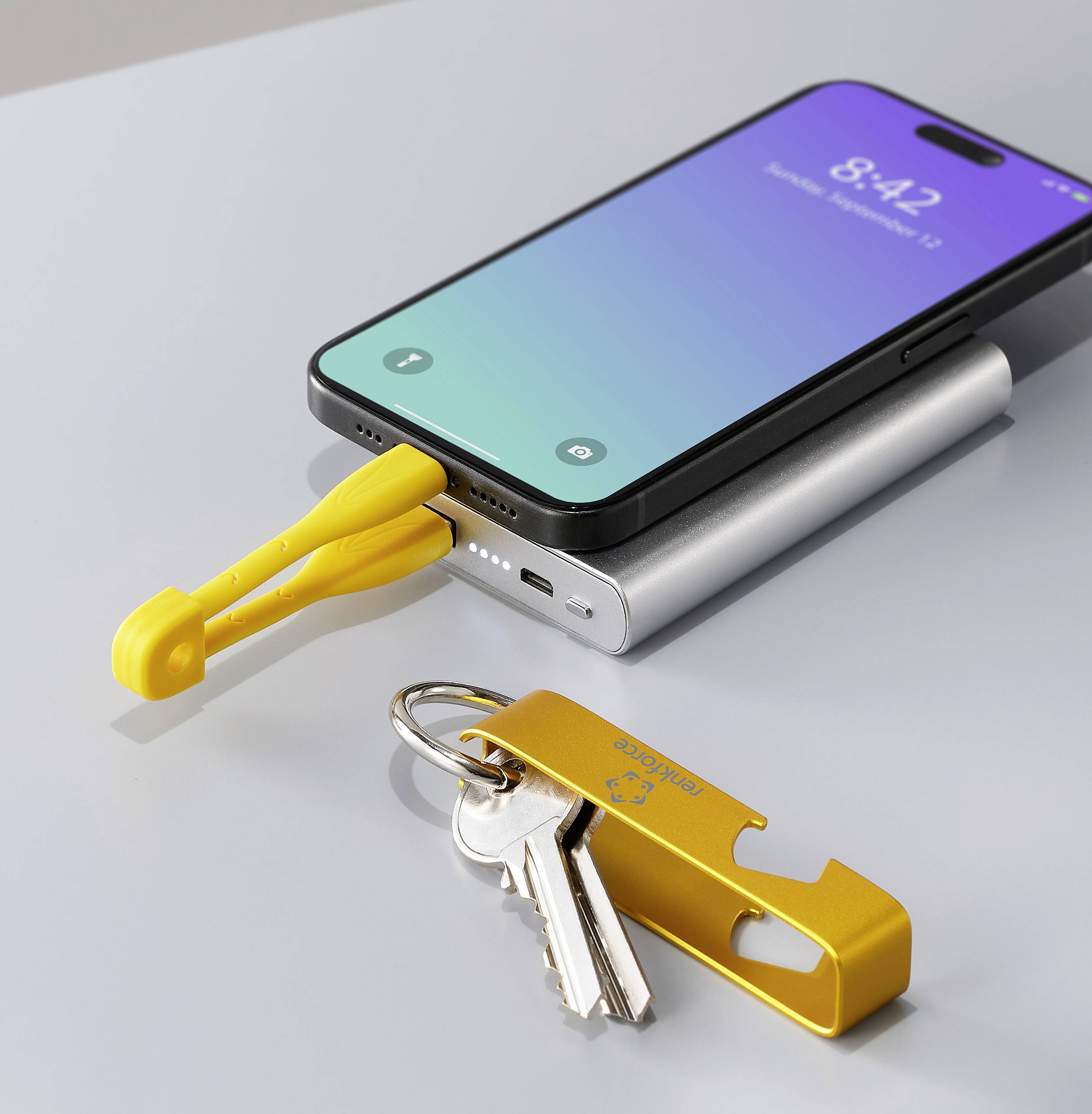 Een smartphone wordt aangesloten op een powerbank met een geel USB-C-kabel. Ernaast ligt een sleutelbos met een gele sleutelhanger.