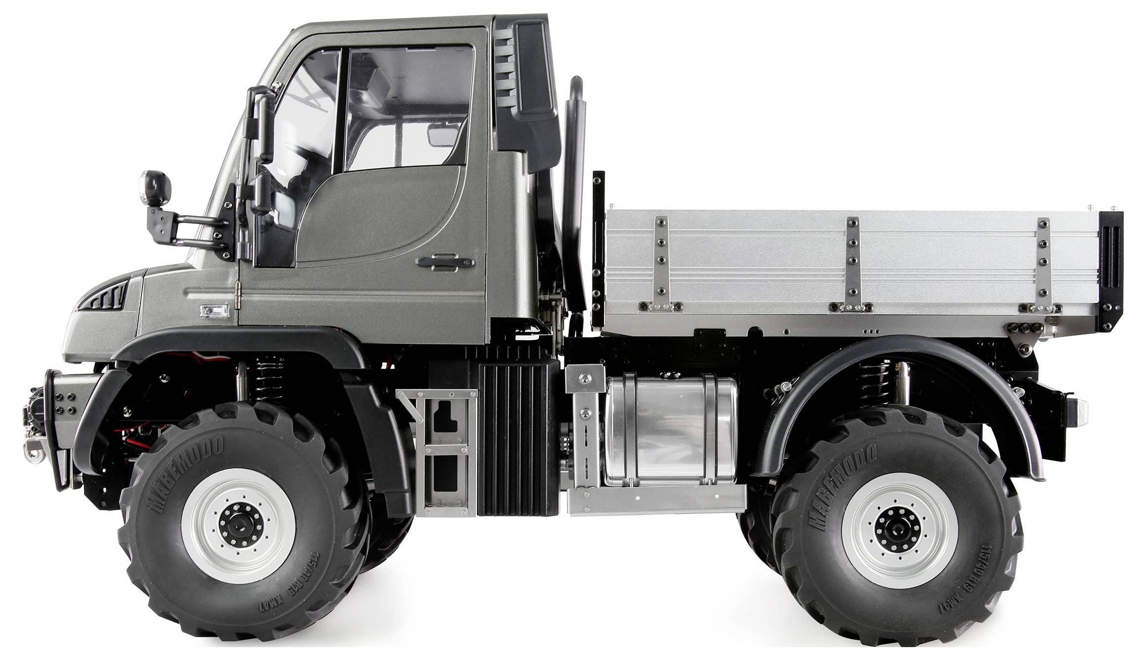 Een zilveren Unimog met grote bodemvrijheid, een gebroken buitenspiegel en een open laadruimte, gefotografeerd van opzij.