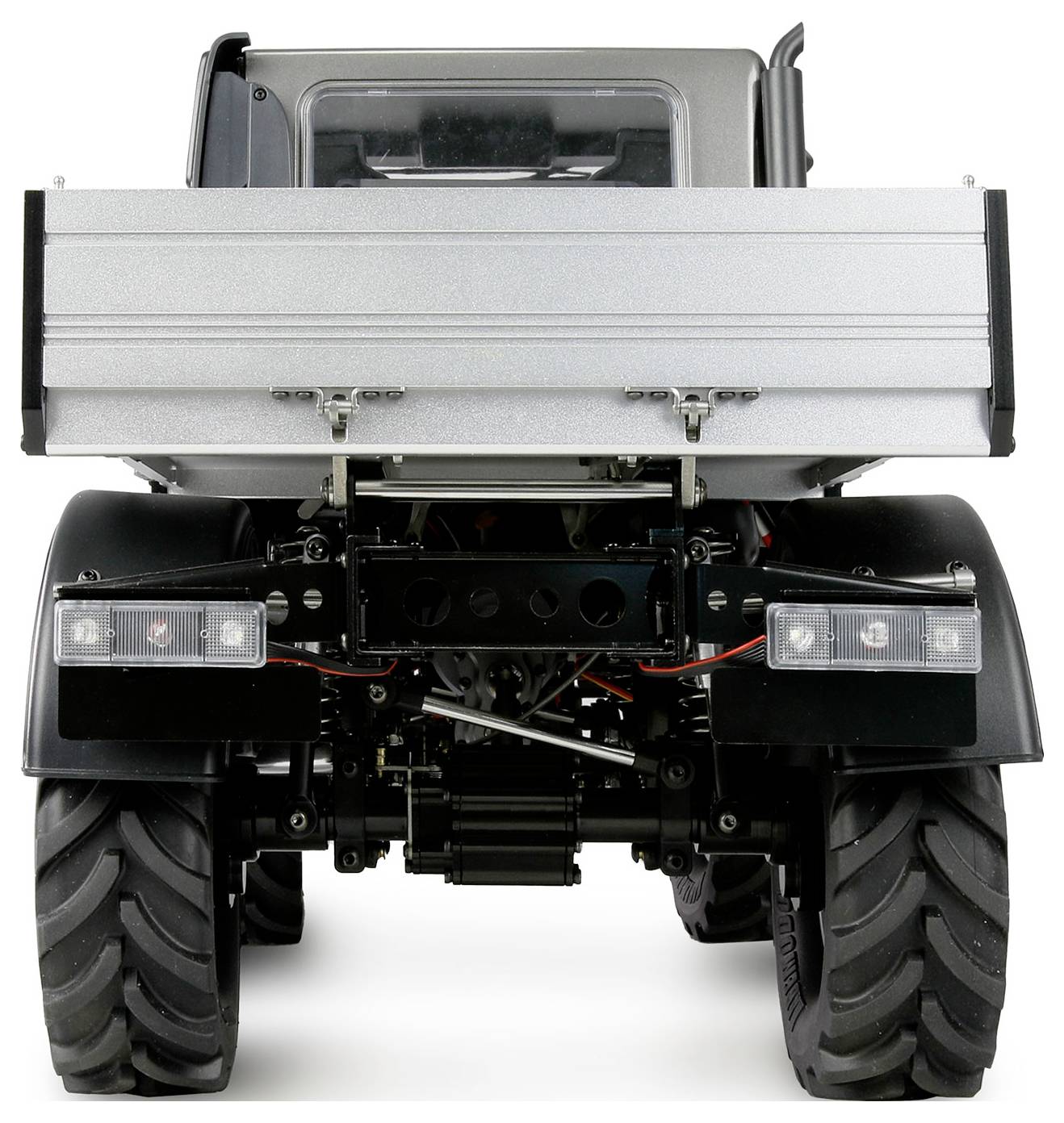 Achteraanzicht van een tractor met een lege, omhoog geklapte aanhanger. Zicht op robuuste achterwielen en voertuigstructuur.