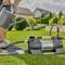 Een persoon begiet een gazon met een gieter, waarbij een elektrische waterpomp op de voorgrond is aangesloten.